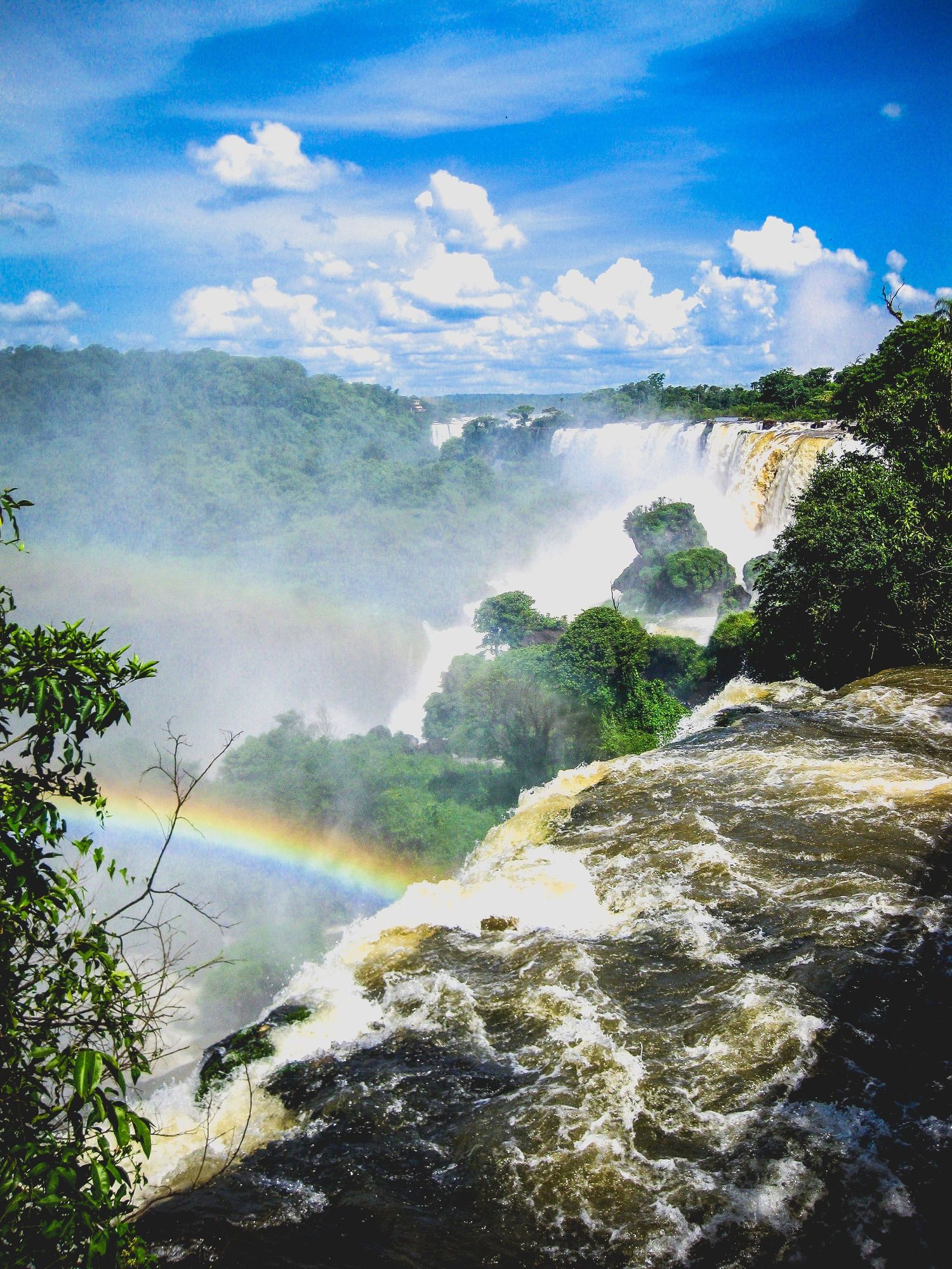 Powerful waterfall creates rainbow mist among lush jungle vegetation at Iguazu Falls.