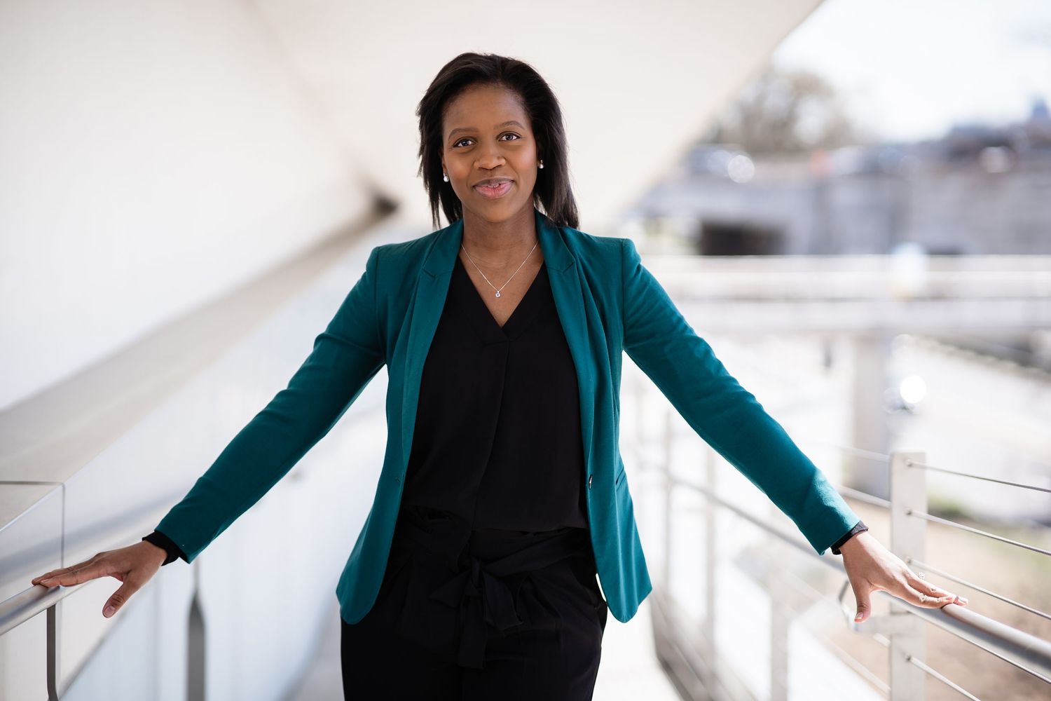 Professional wearing a teal blazer and black top poses confidently against a light background.