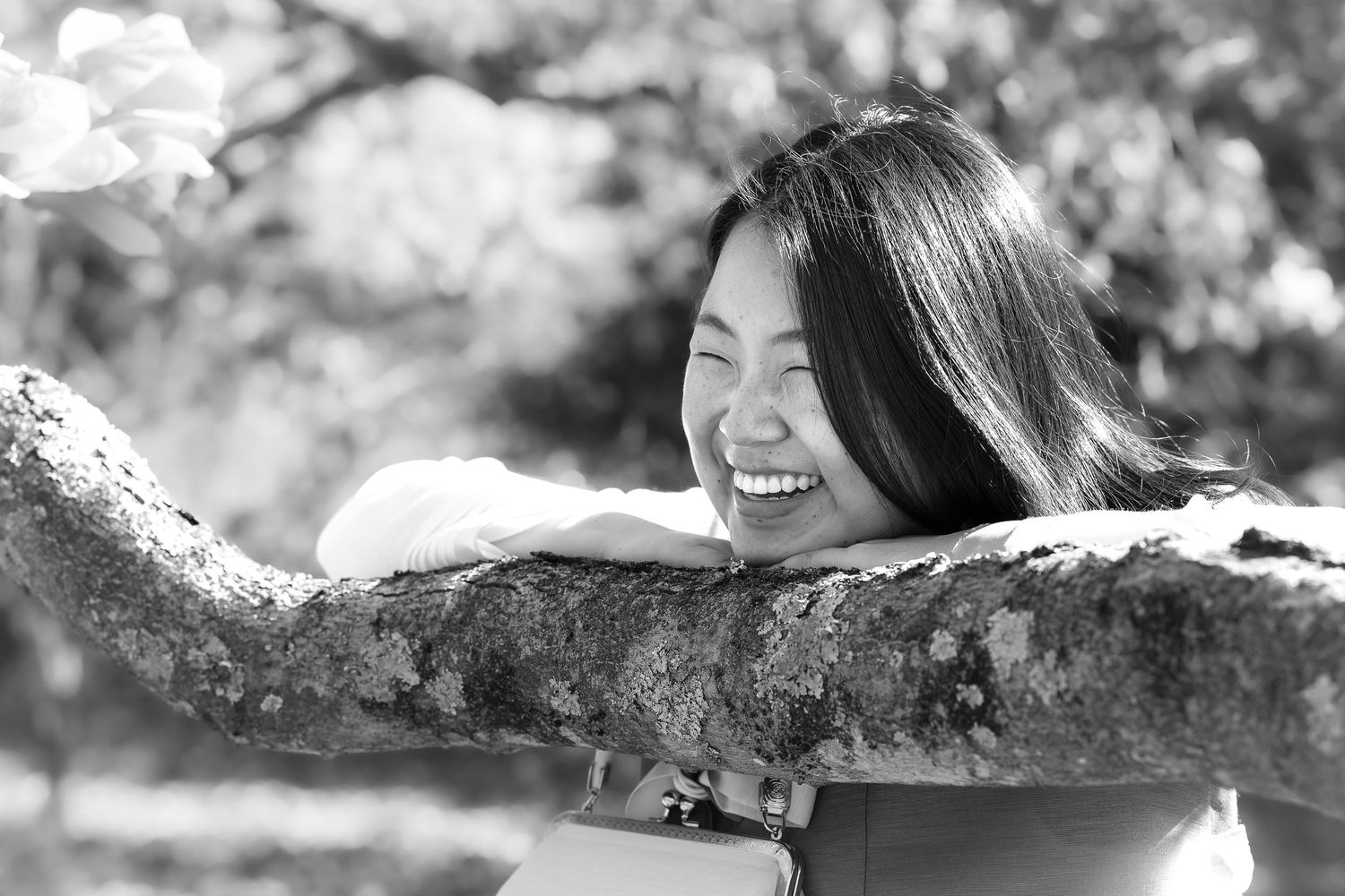 Black and white portrait of person joyfully resting on tree branch.