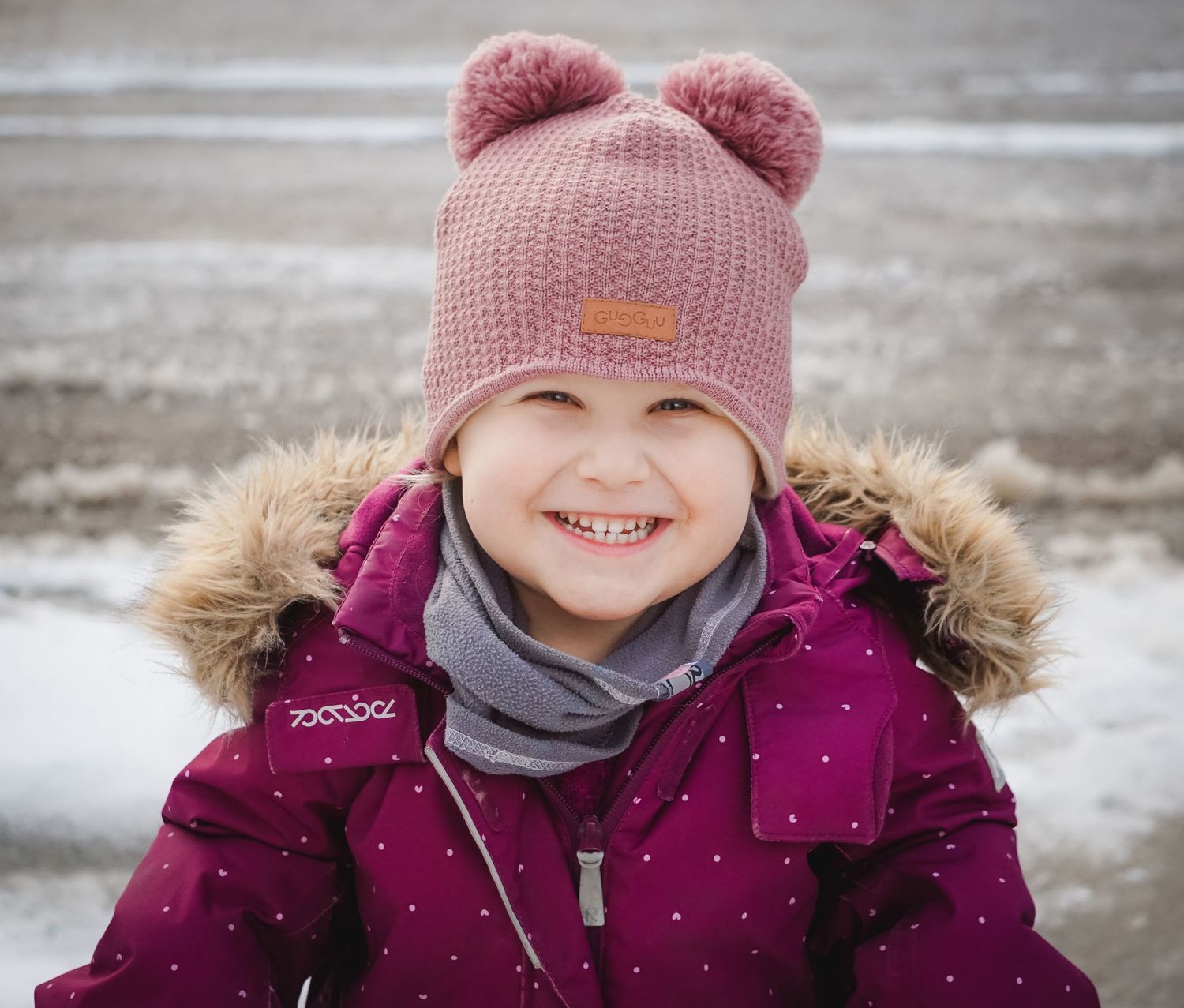 Child wearing pink winter hat and purple coat in snowy weather.