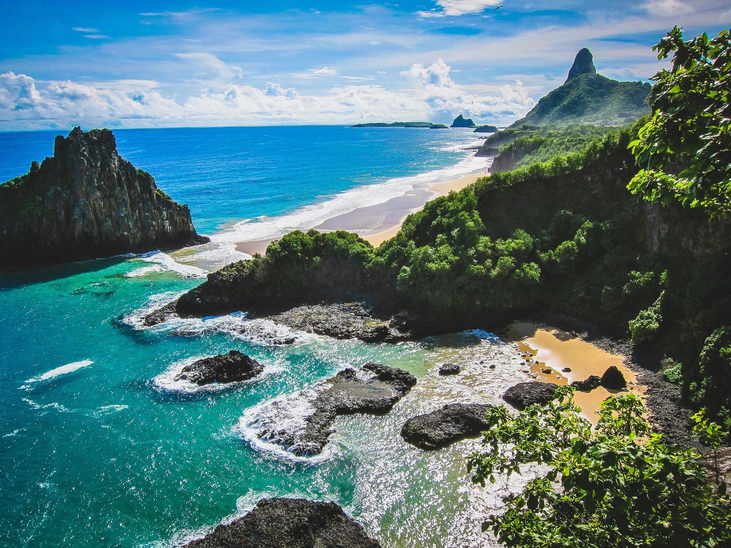 Dramatic coastal cliffs meet turquoise waters under bright blue skies along a tropical shoreline.
