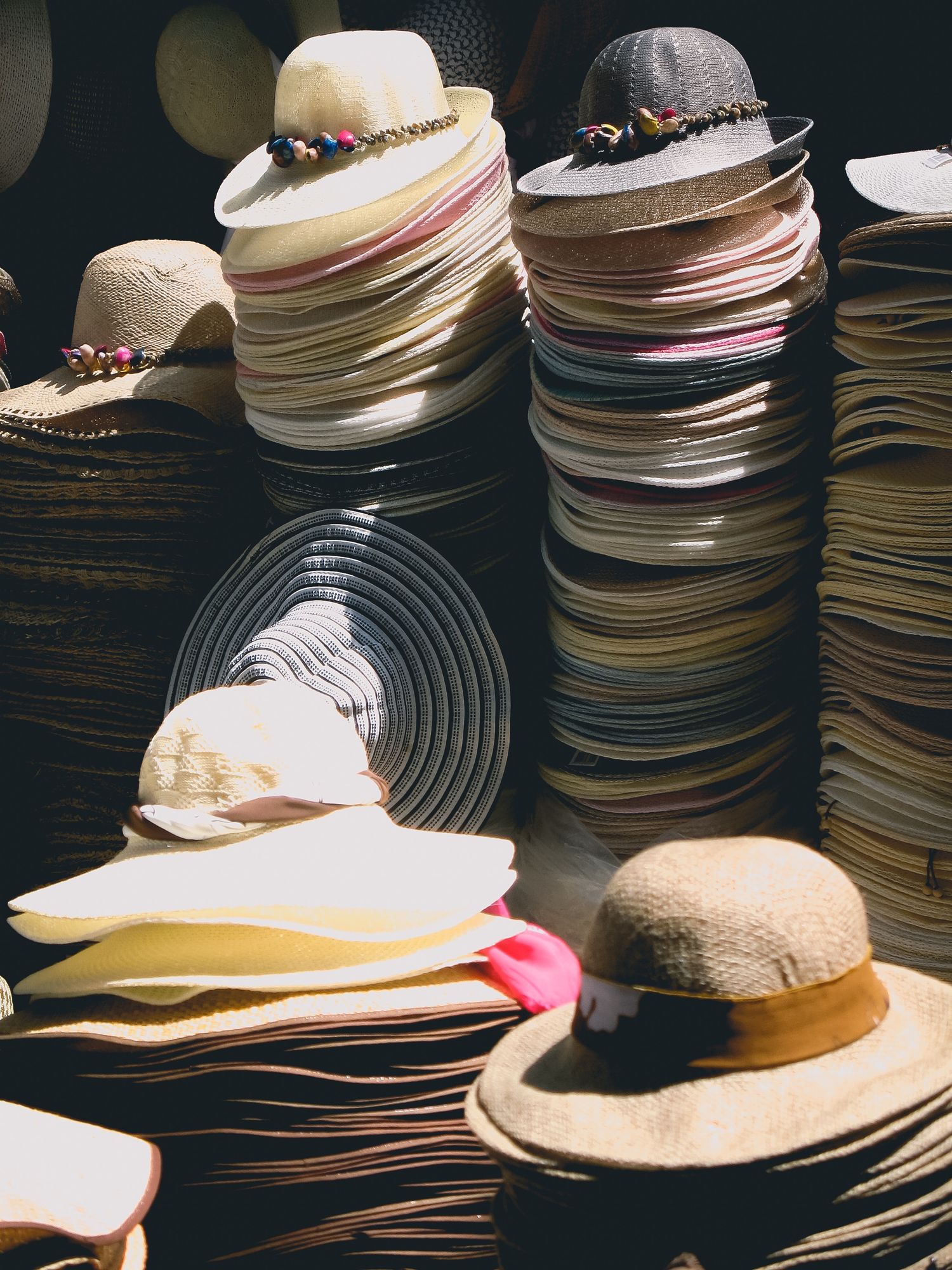 Stacks of vintage sun hats with ribbons and bands displayed in layers.