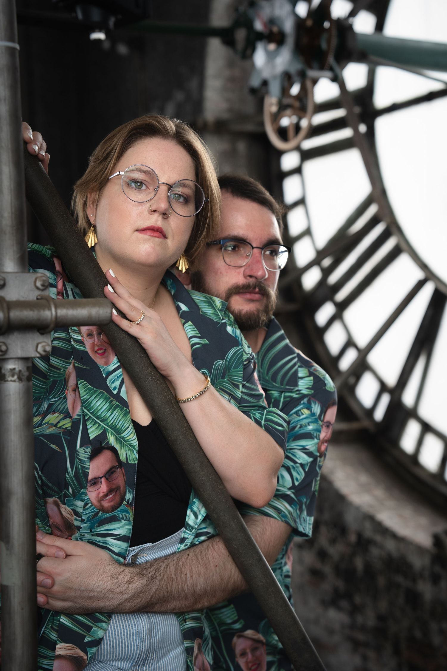 A couple in matching tropical print shirts pose against a clock tower backdrop.