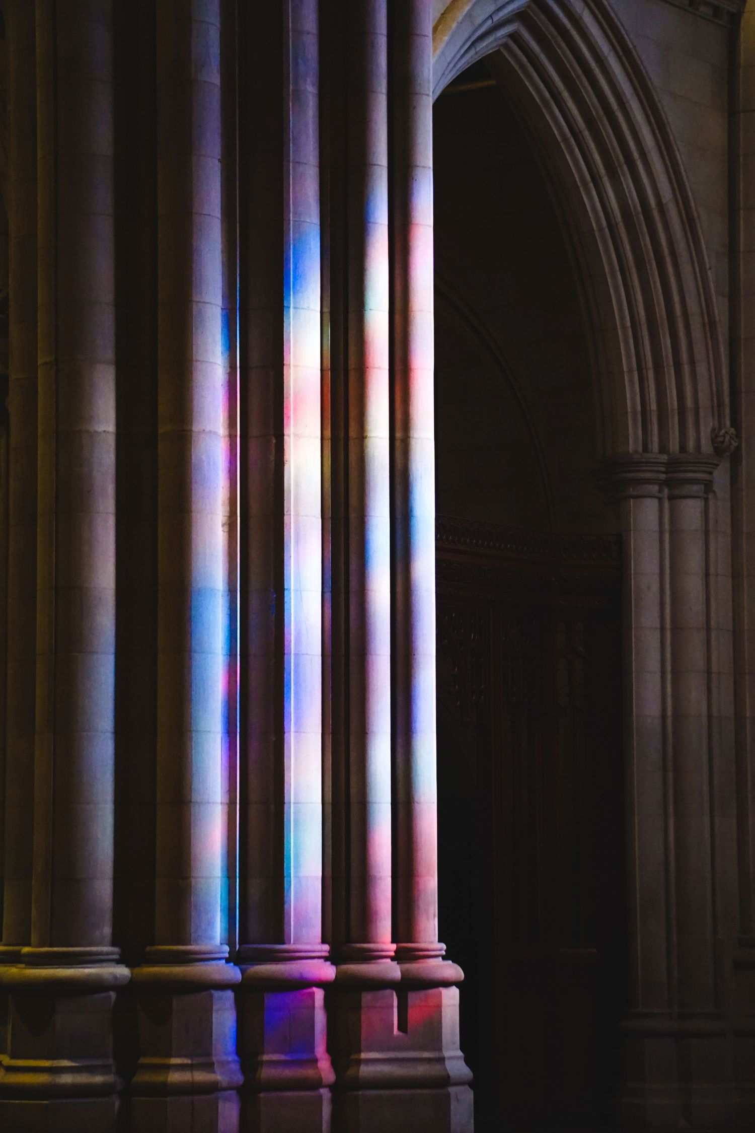 Gothic church columns illuminated with colorful rainbow light streaming through stained glass.
