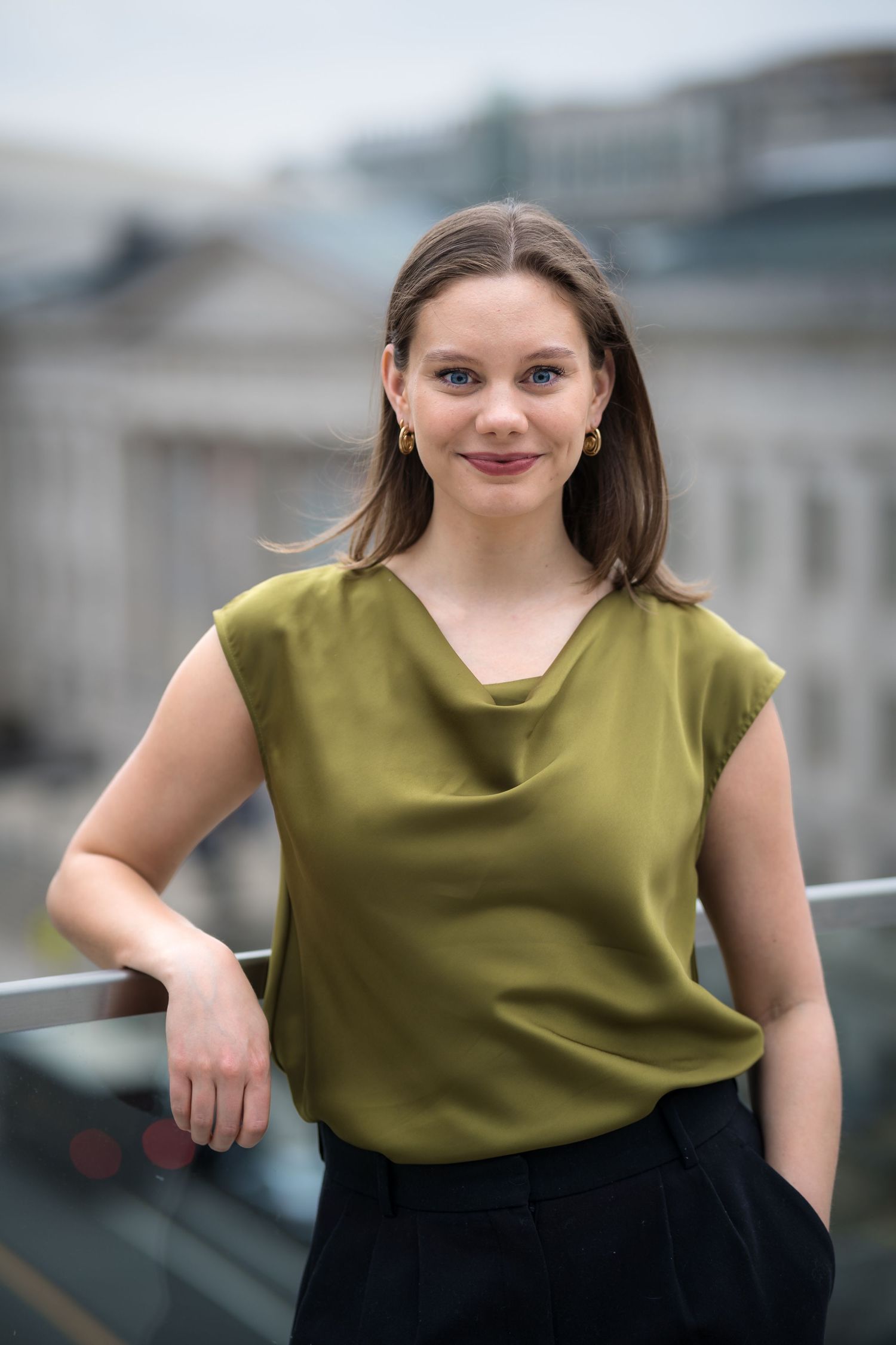 Professional headshot portrait of someone wearing an olive green sleeveless top against a blurred background.
