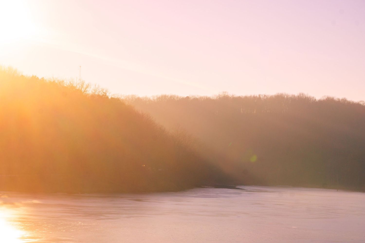 Misty golden sunrise over a serene lake with silhouetted hills in the background.