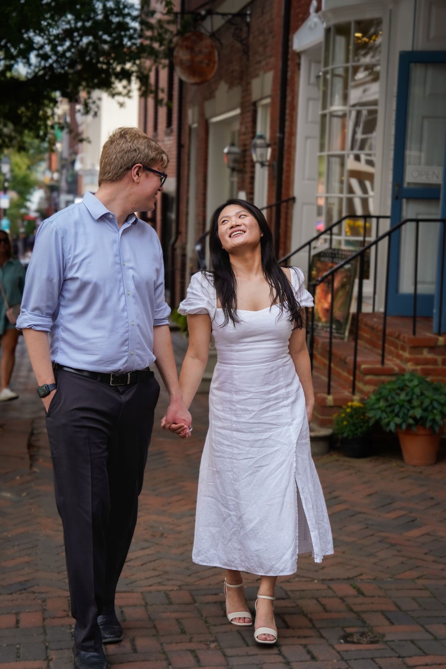 A couple walks hand in hand along a brick-paved street with historic buildings.