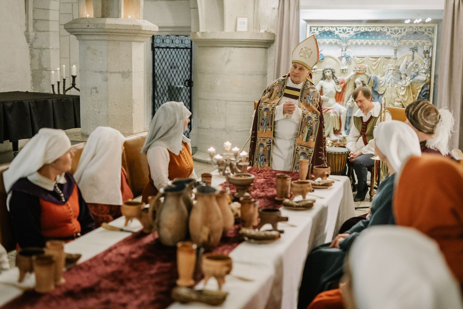 Medieval banquet reenactment with costumed guests seated at a decorated table in a historic stone hall.