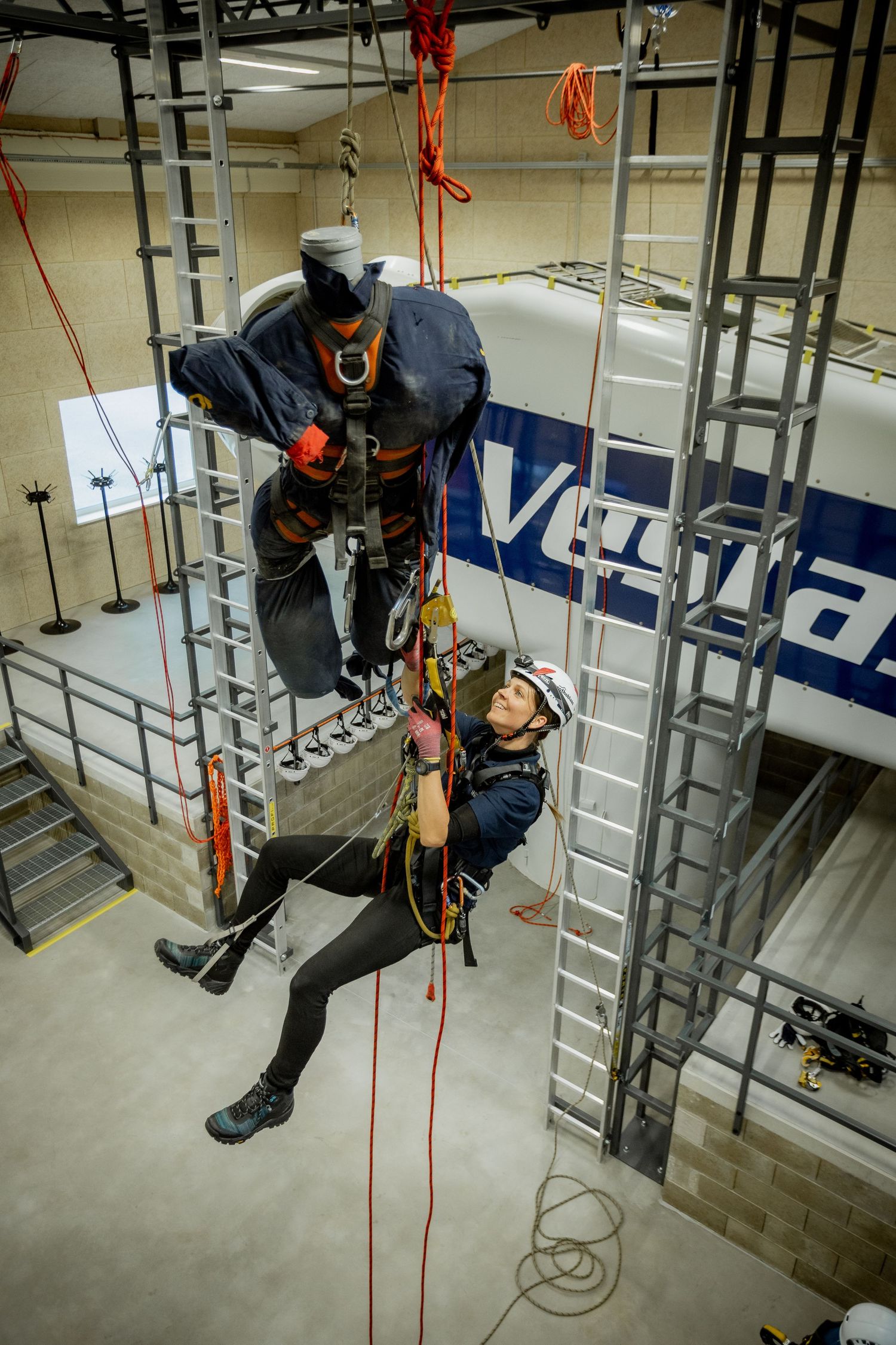 Two workers in safety harnesses practicing rope rescue techniques on an indoor climbing structure during training.