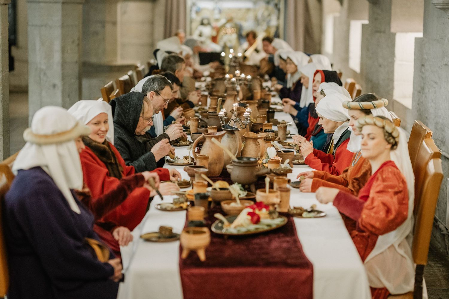 People in medieval costumes dining at a long banquet table with candles and wooden bowls at a historical reenactment.