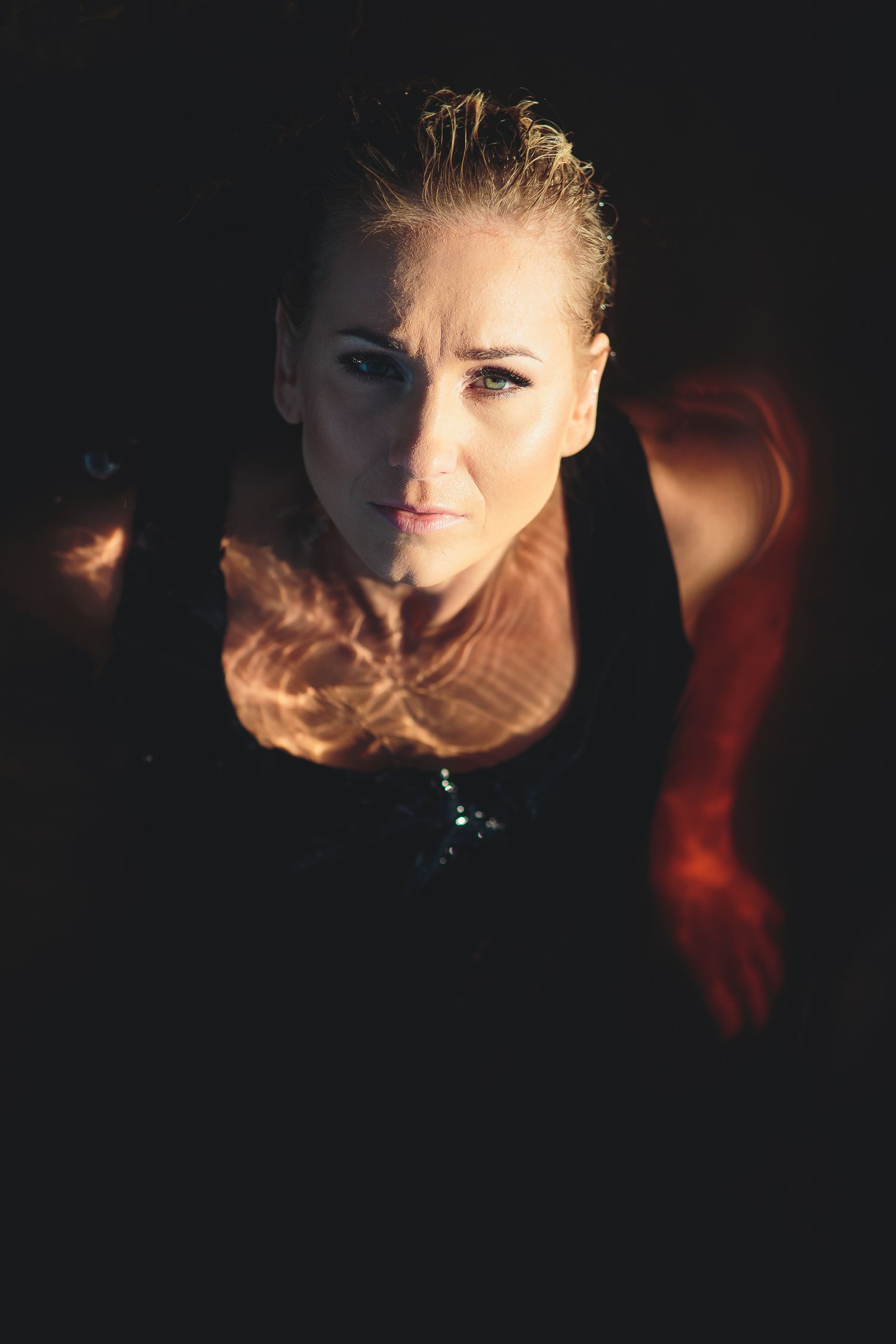 Intense close-up portrait of athletic blonde woman with dramatic lighting and dark background.
