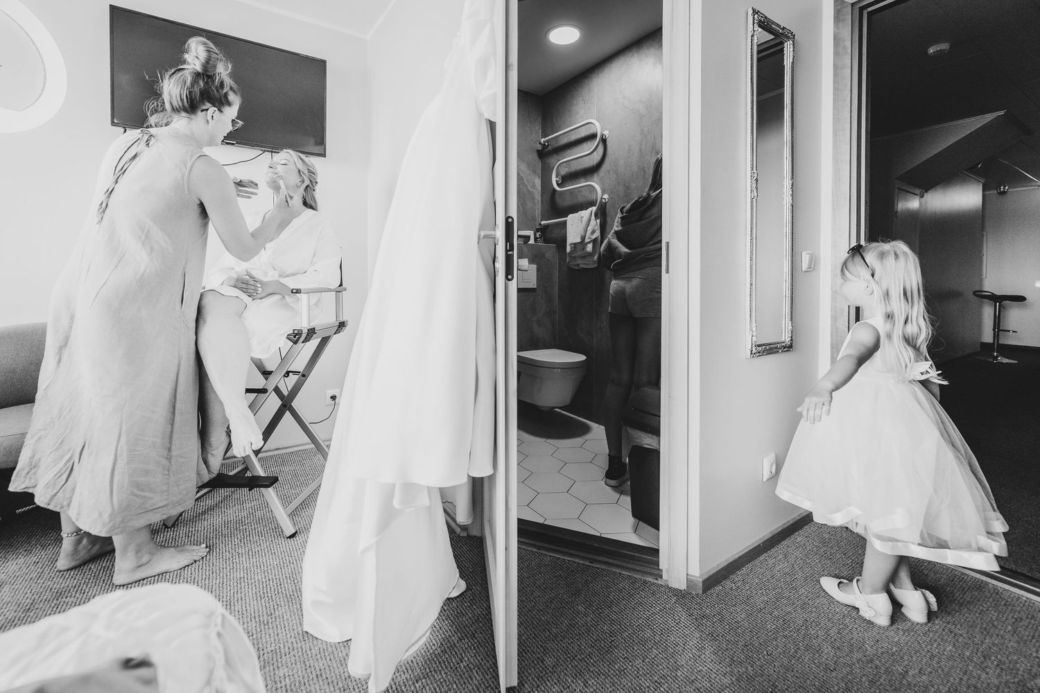 Black and white wedding preparation photo showing bride being dressed while flower girl waits in doorway.