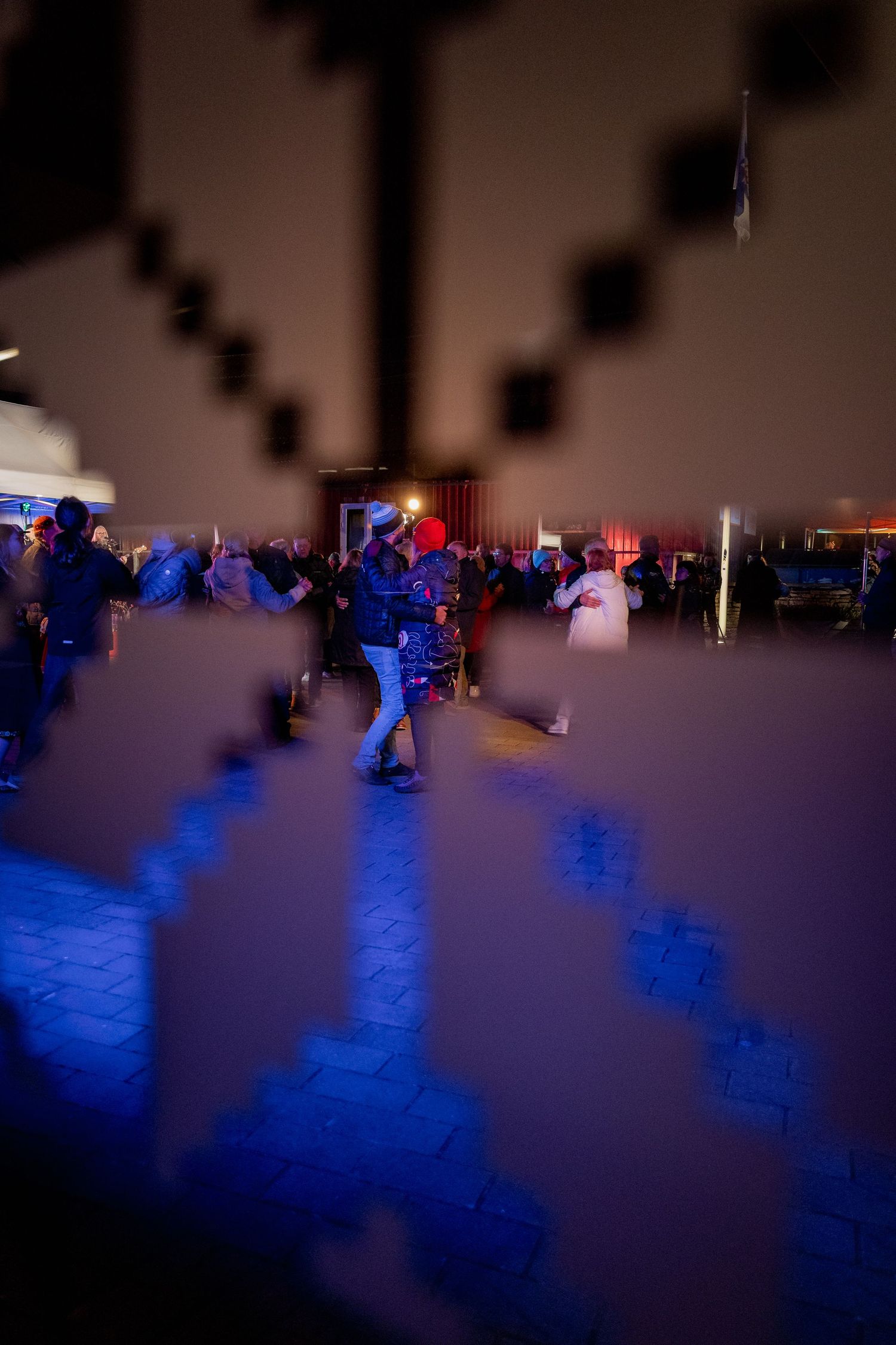 People dancing at an outdoor night event illuminated by blue lights in winter.
