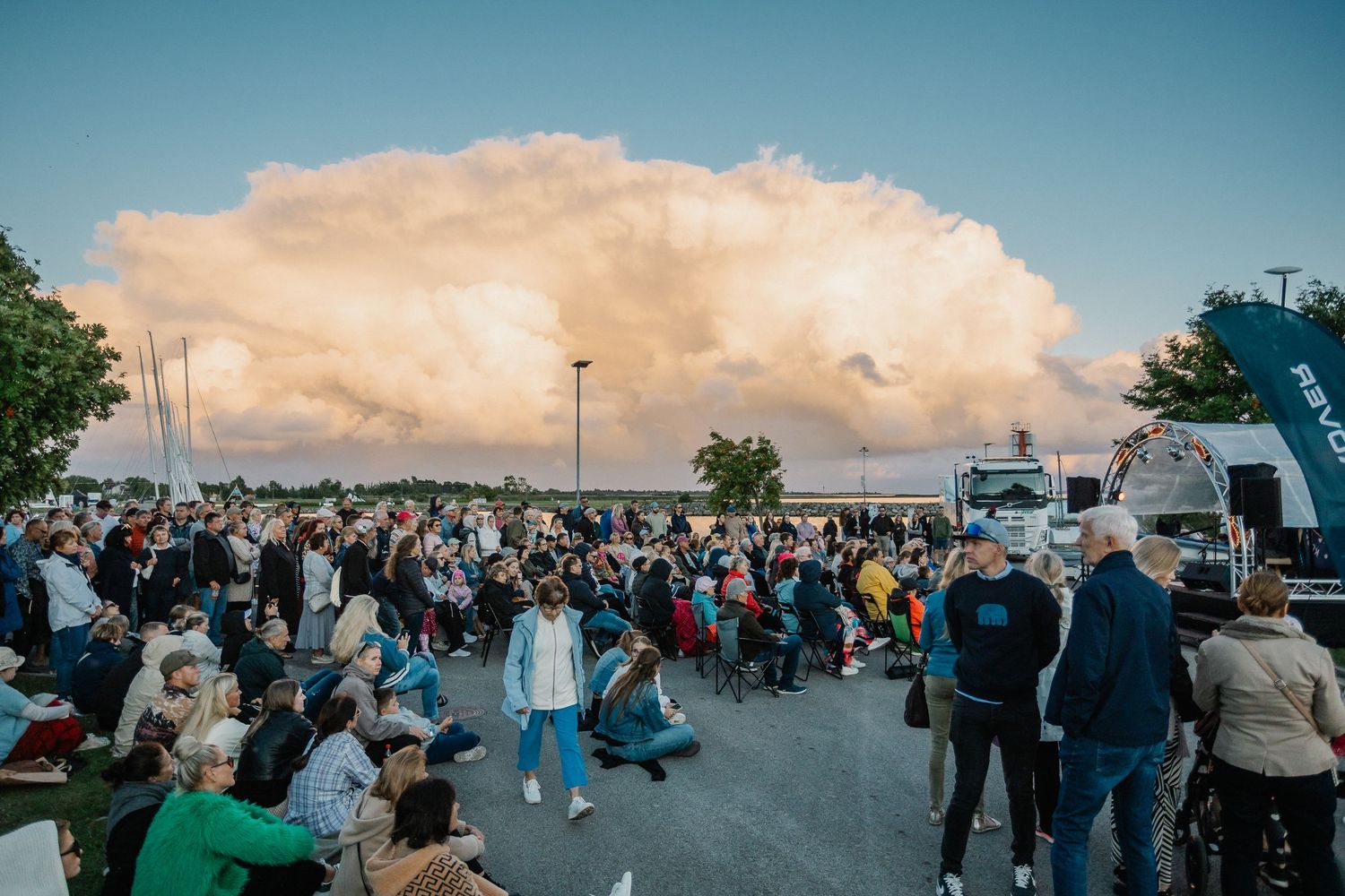 Large crowd gathered outdoors watching a dramatic mushroom cloud formation in the sky at dusk.