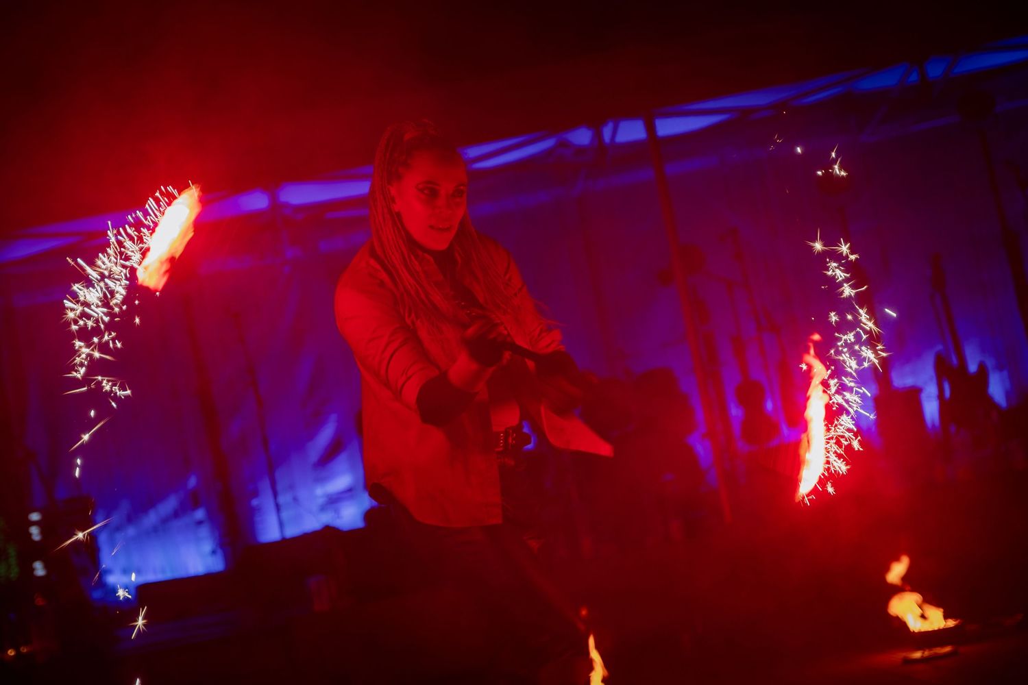 Performer surrounded by dramatic red and blue lights with sparkling pyrotechnics during an intense live show.