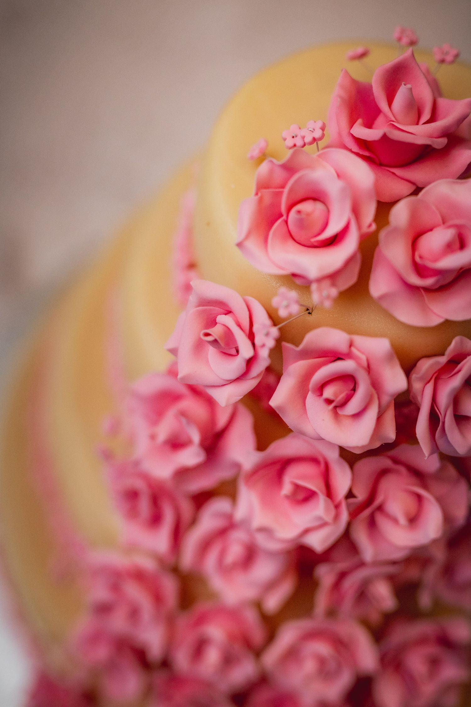 Close-up of a tiered wedding cake decorated with pink sugar roses and small floral accents on yellow fondant.