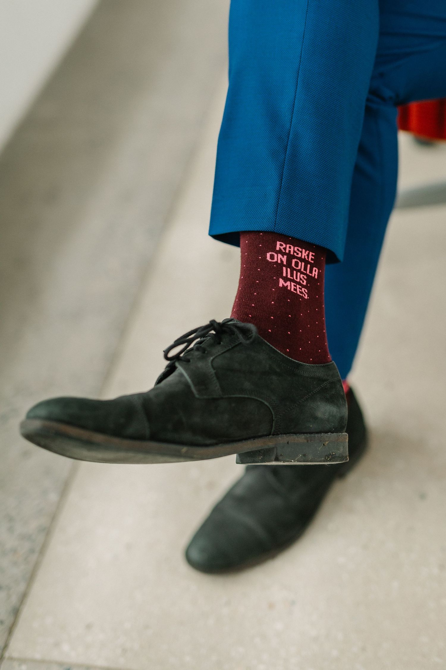 Close-up of blue trousers, dark suede oxford shoes, and burgundy socks with text pattern.