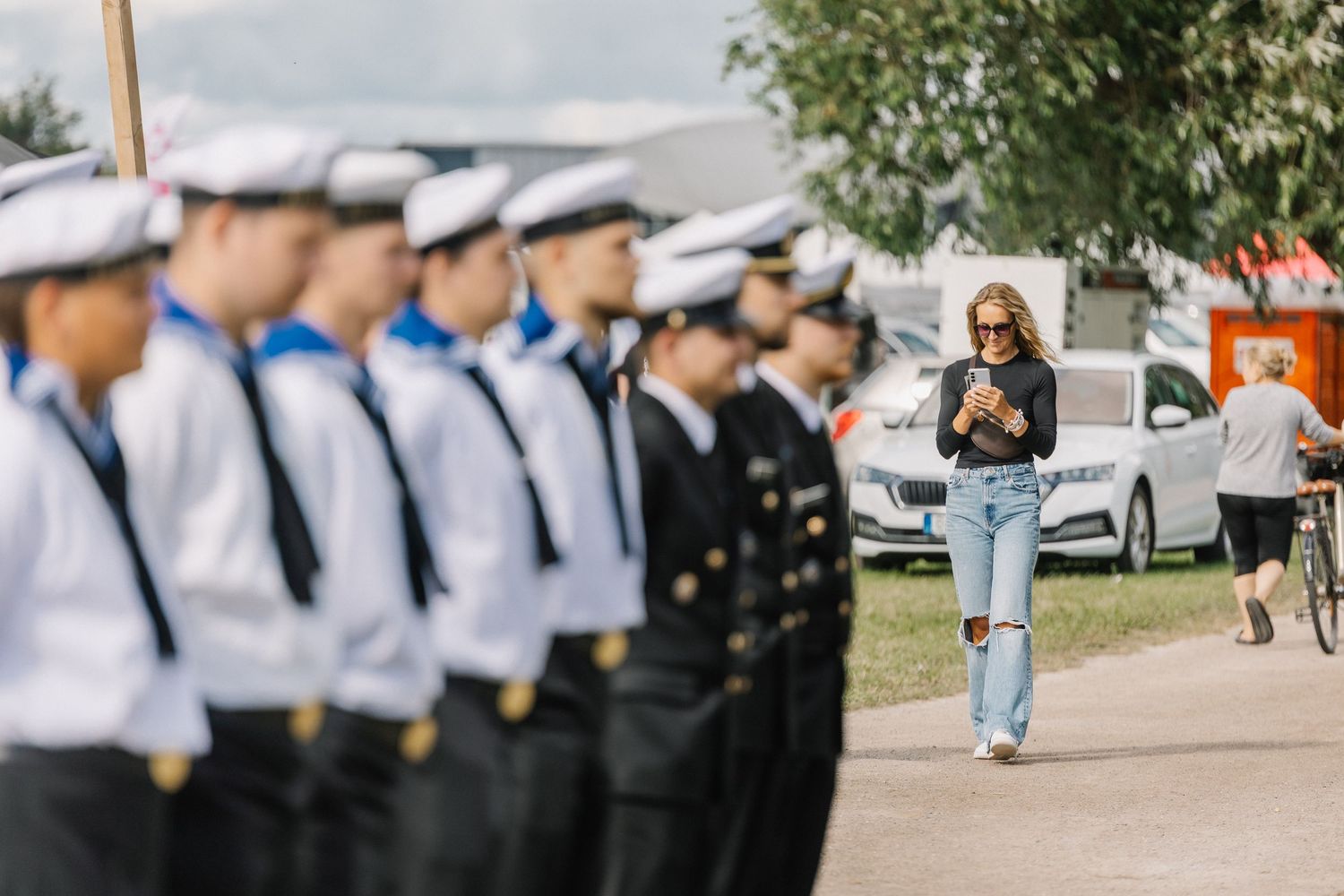 Row of naval officers in uniform standing at attention as a woman walks past on a sunny day.