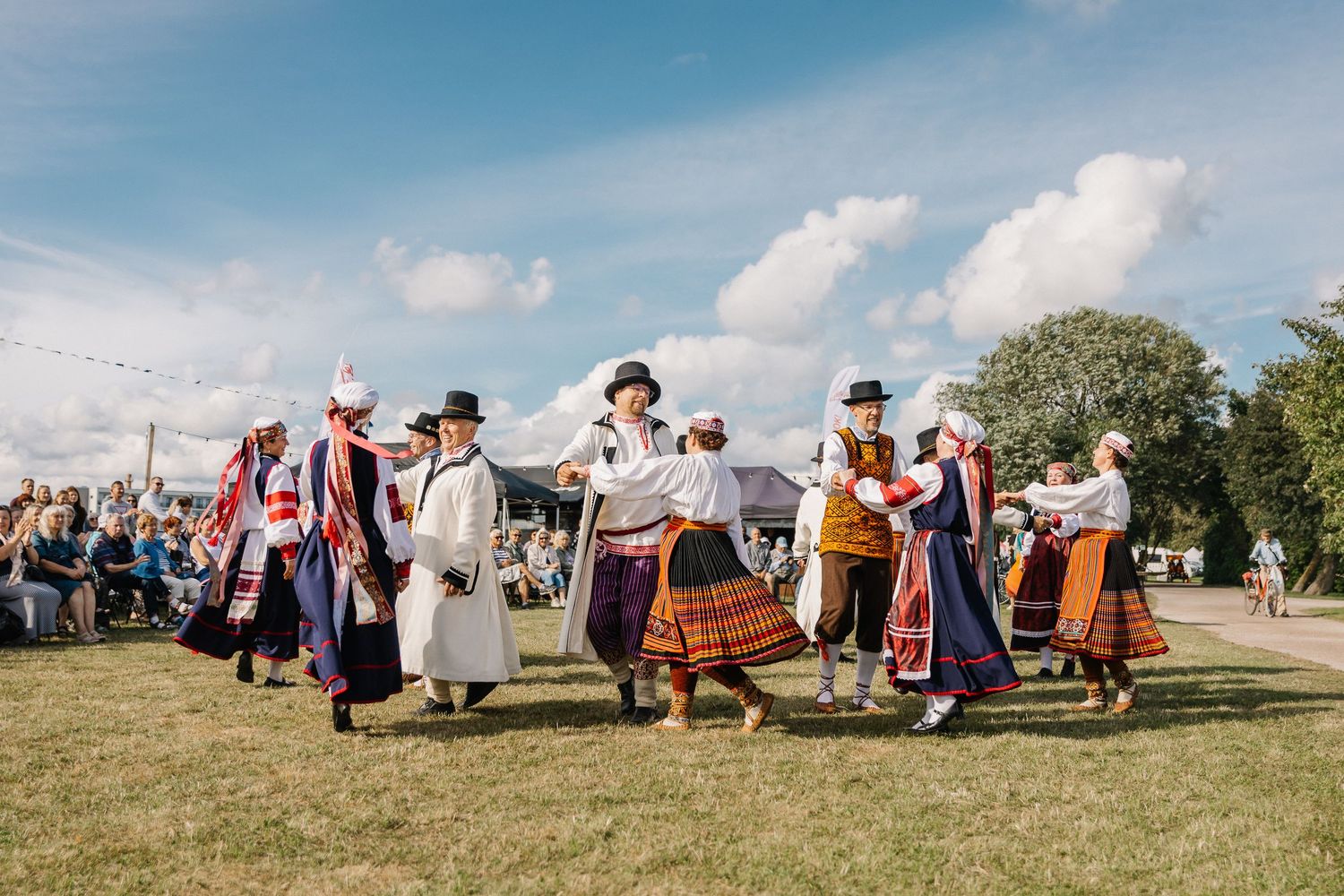 Traditional Estonian folk dancers in colorful national costumes performing outdoors at a summer festival.
