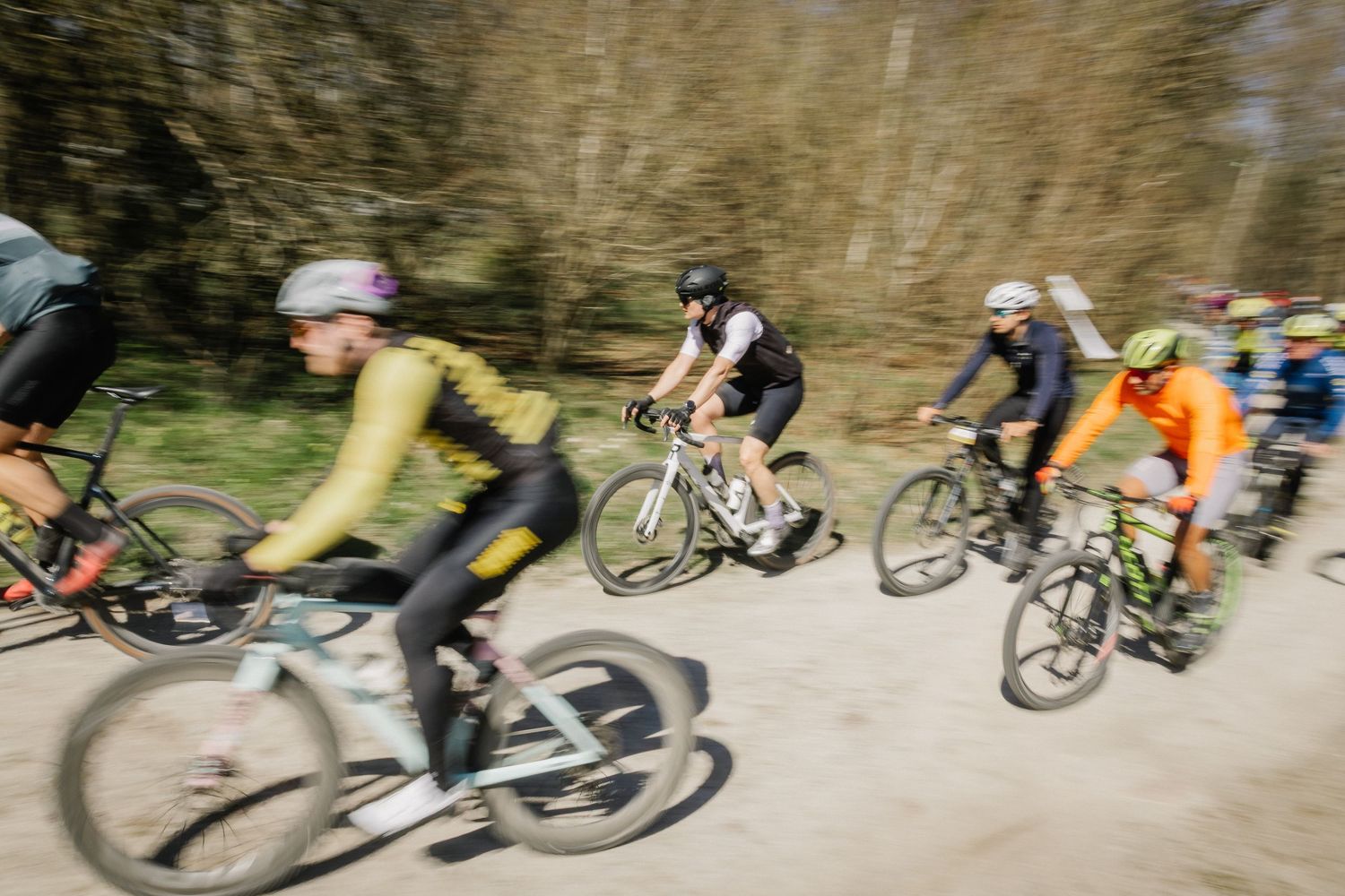 Group of cyclists racing on a dirt trail through a forest during a mountain bike race event.