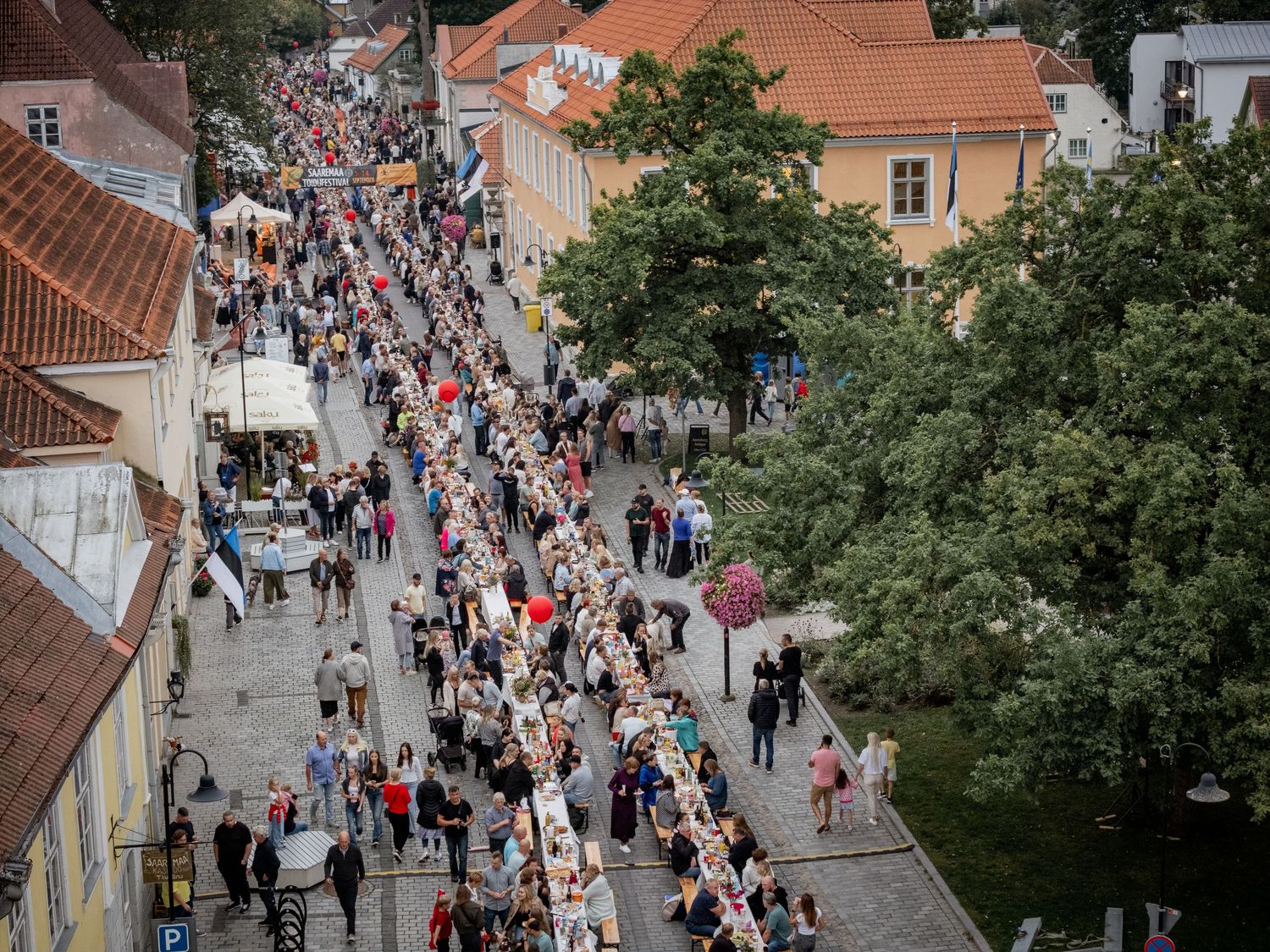 Aerial view of a large outdoor street dining event with crowds of people along a long table in a historic European town.