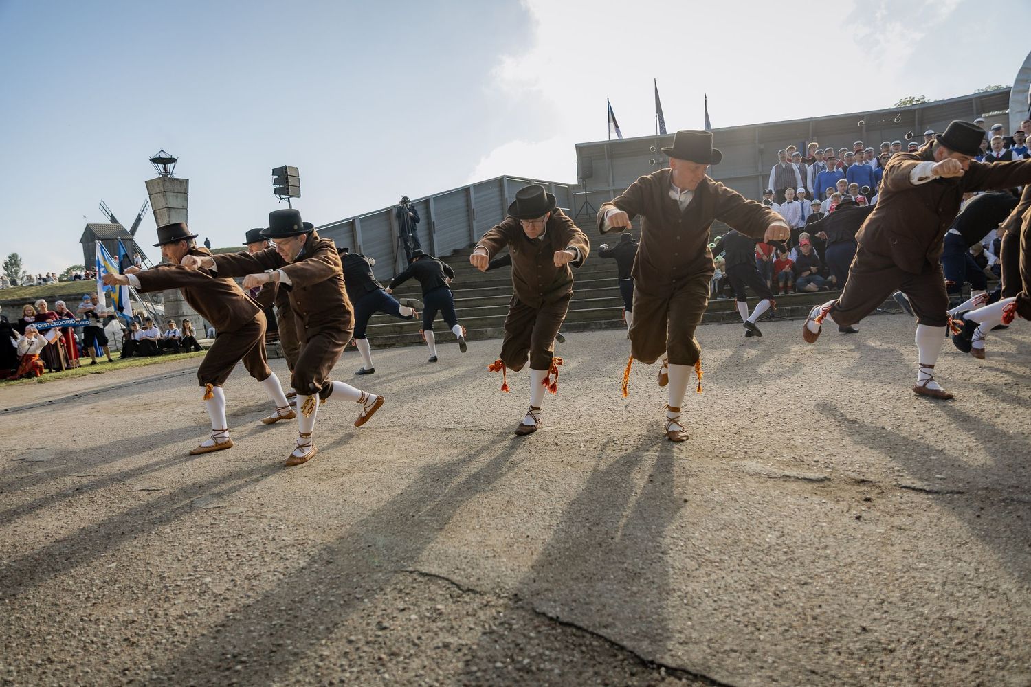 Men in traditional Bavarian lederhosen perform an energetic folk dance outdoors at Oktoberfest celebration.