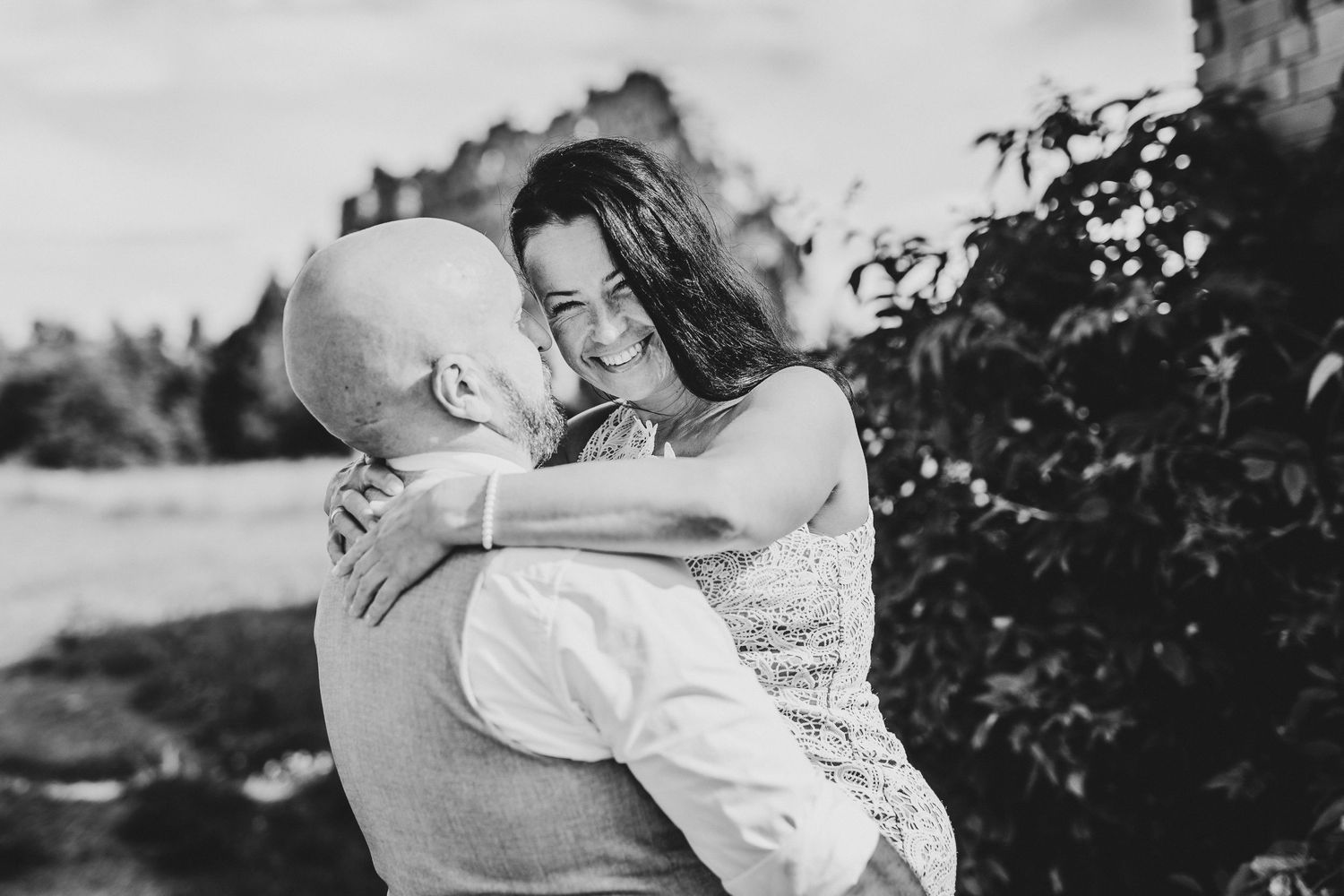 Black and white photo of a couple embracing outdoors, woman smiling joyfully as man kisses her cheek.