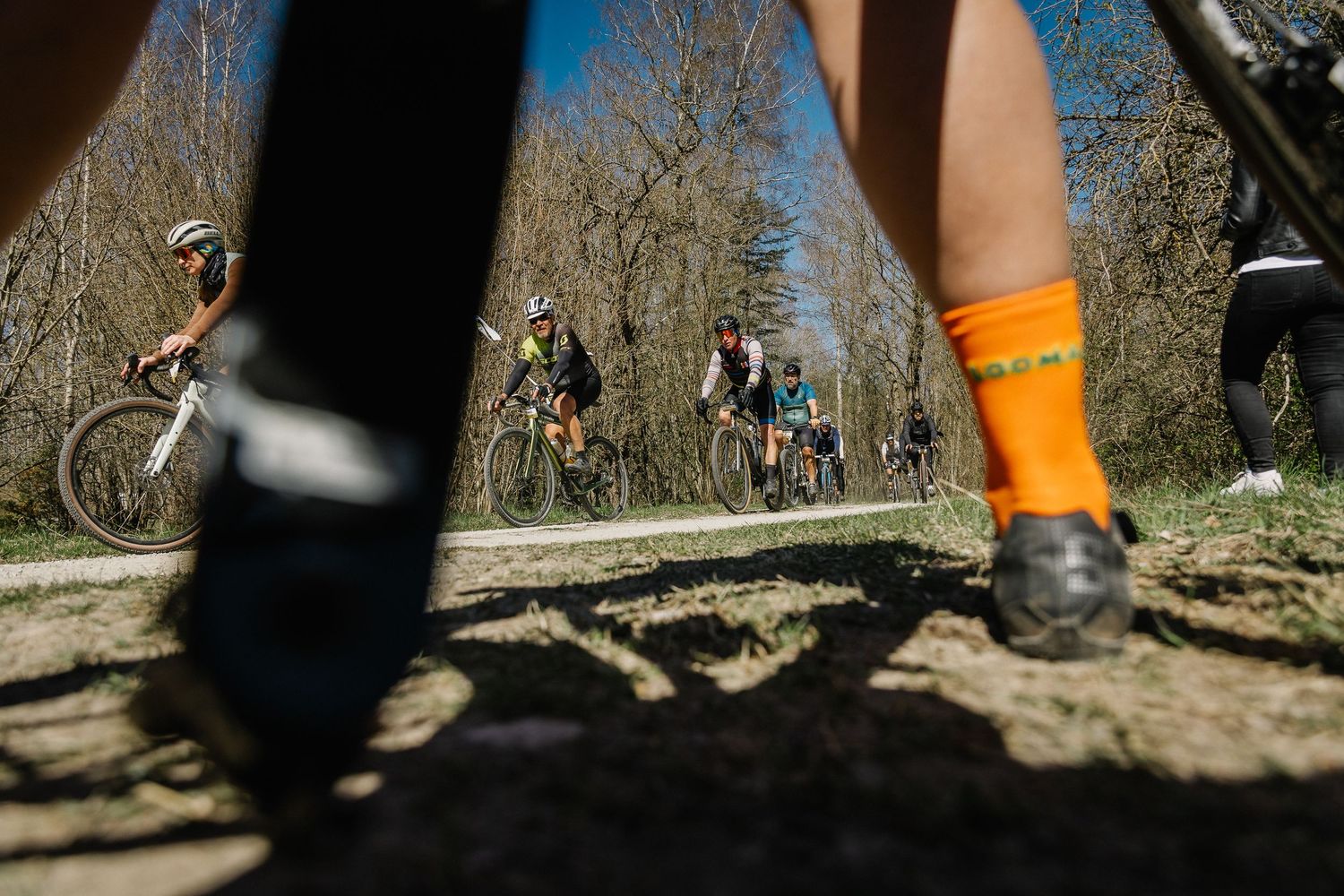 Low-angle view of cyclists racing on a dirt path through a sunny forest during a mountain bike race.
