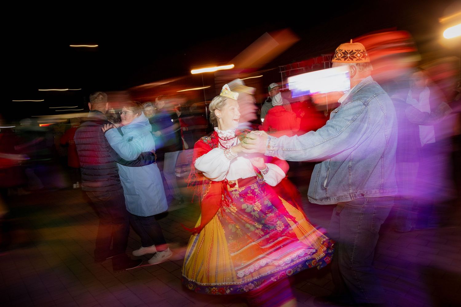 Blurred motion photo of people dancing in traditional Russian folk costumes at a lively cultural celebration.