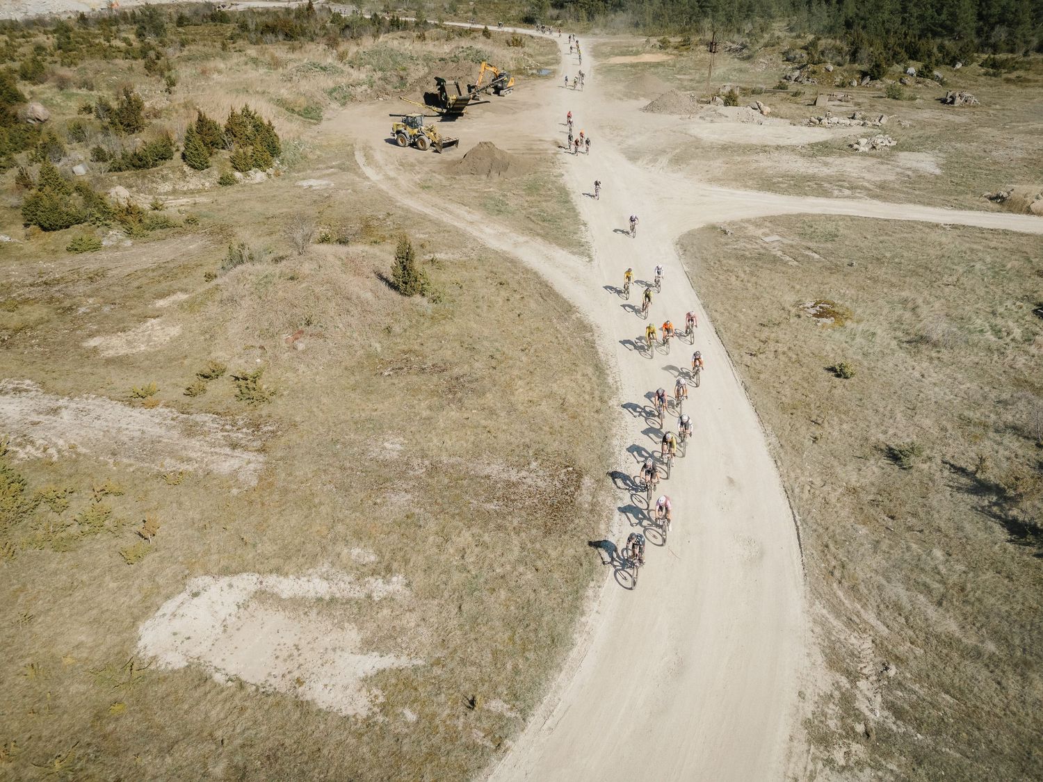 Aerial view of cyclists riding along a winding dirt trail through an arid landscape with sparse trees.