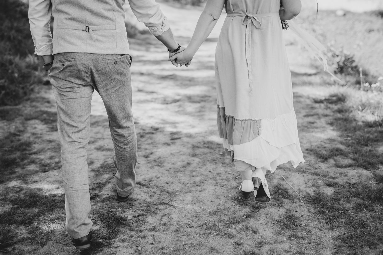 Black and white photo of a couple holding hands while walking on a path, woman in flowing dress.