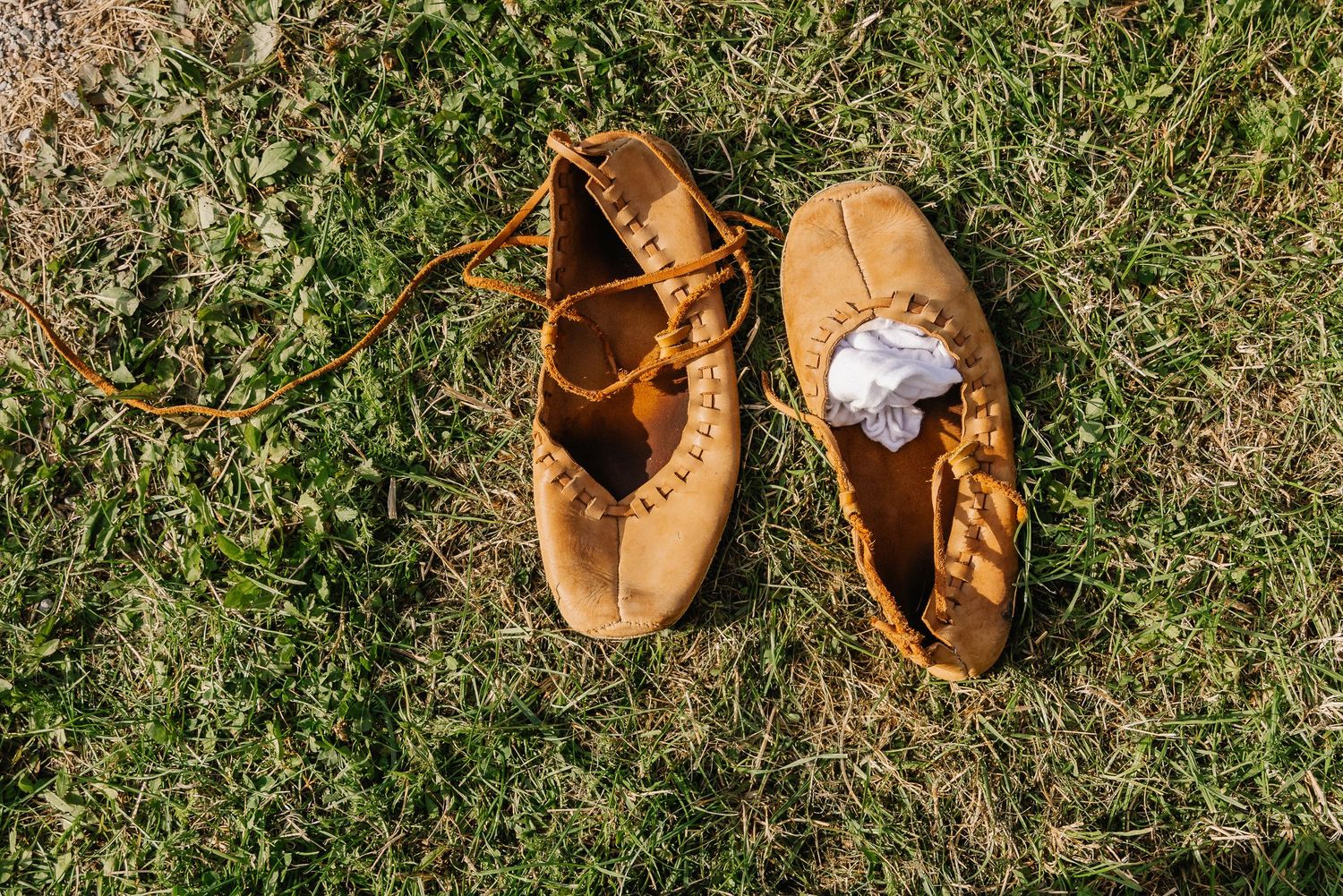 Tan leather moccasin shoes with lace ties resting on green grass outdoors.