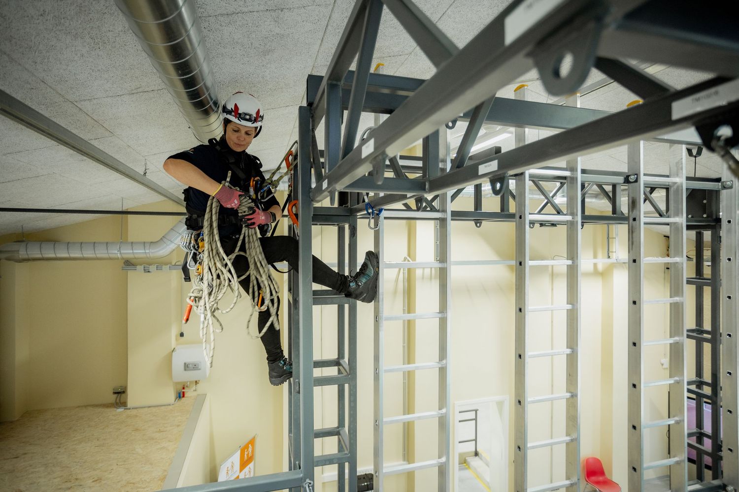 Worker in safety gear climbing metal scaffolding structure indoors during construction or maintenance work.