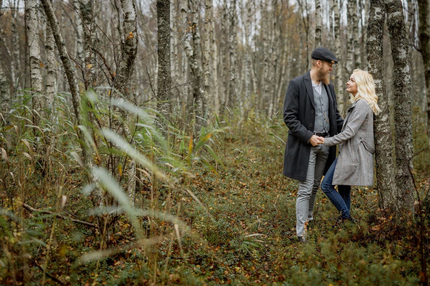 Couple holding hands and gazing at each other while walking through a birch forest in autumn.