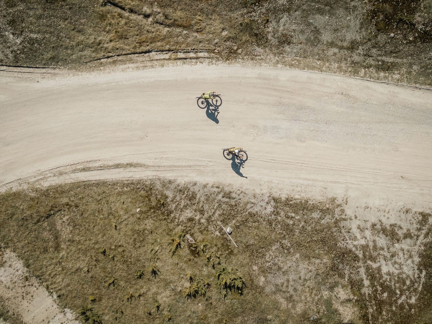 Aerial view of two cyclists riding mountain bikes on a sandy dirt trail path from above.
