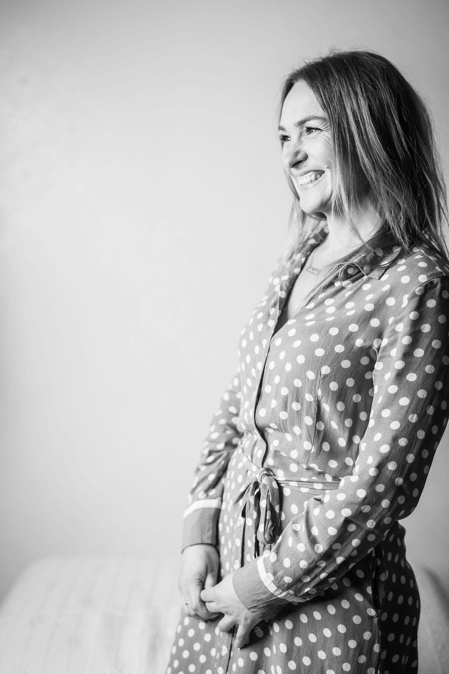 Smiling woman in polka dot dress poses sideways in black and white portrait photo.
