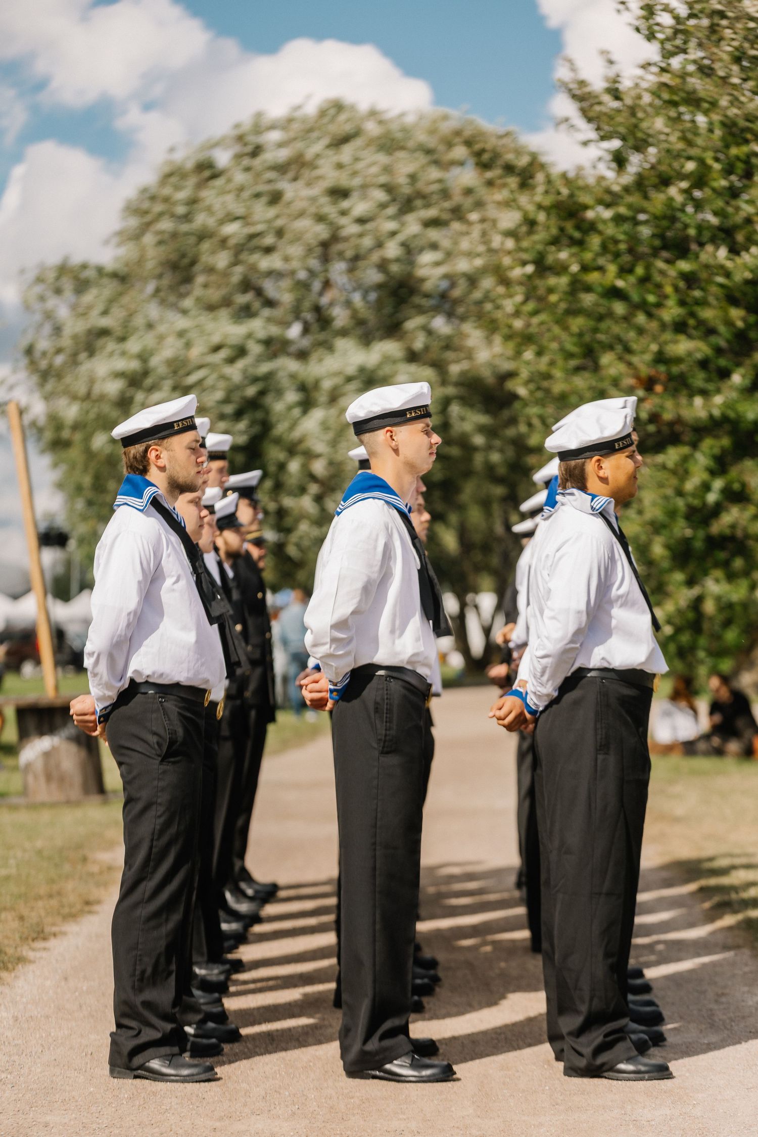 Naval cadets in white caps and uniforms standing at attention in a line outdoors.