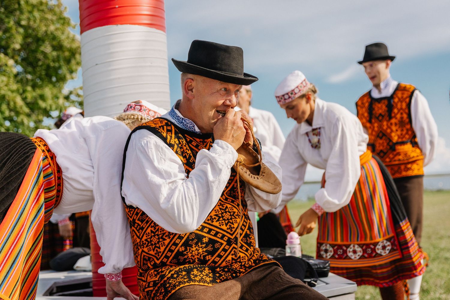 Men in traditional Estonian folk costumes perform at an outdoor cultural festival on a sunny day.