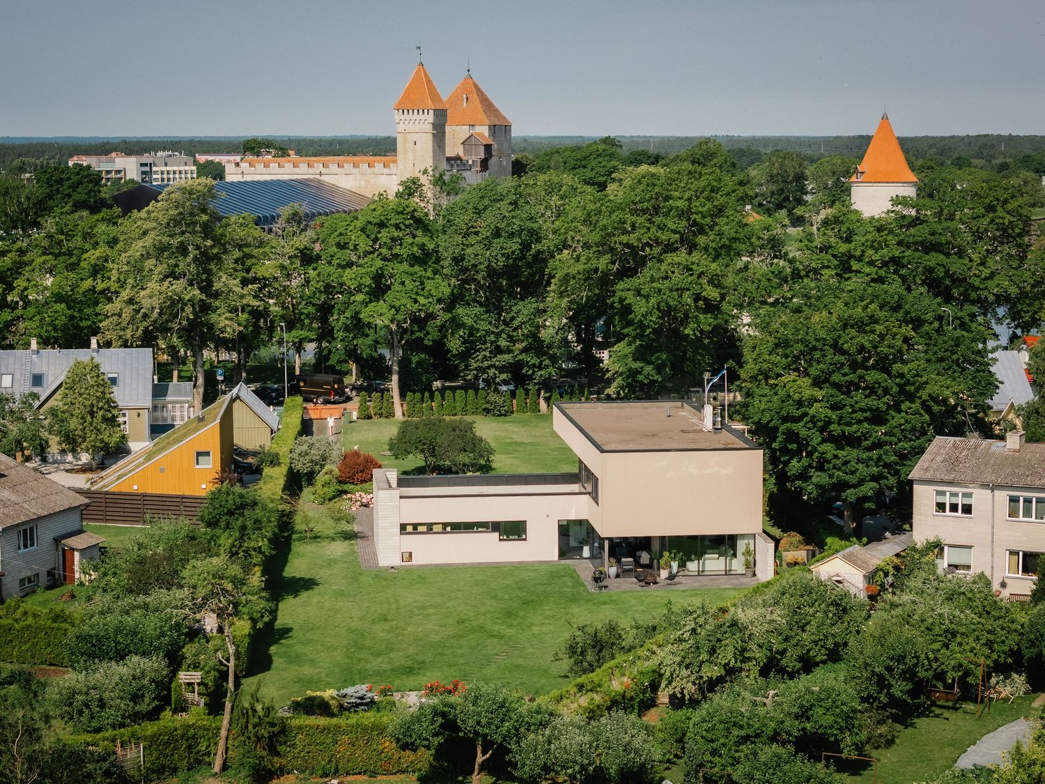 Aerial view of a modern home with green roof surrounded by lush gardens, with medieval castle towers visible beyond the trees.