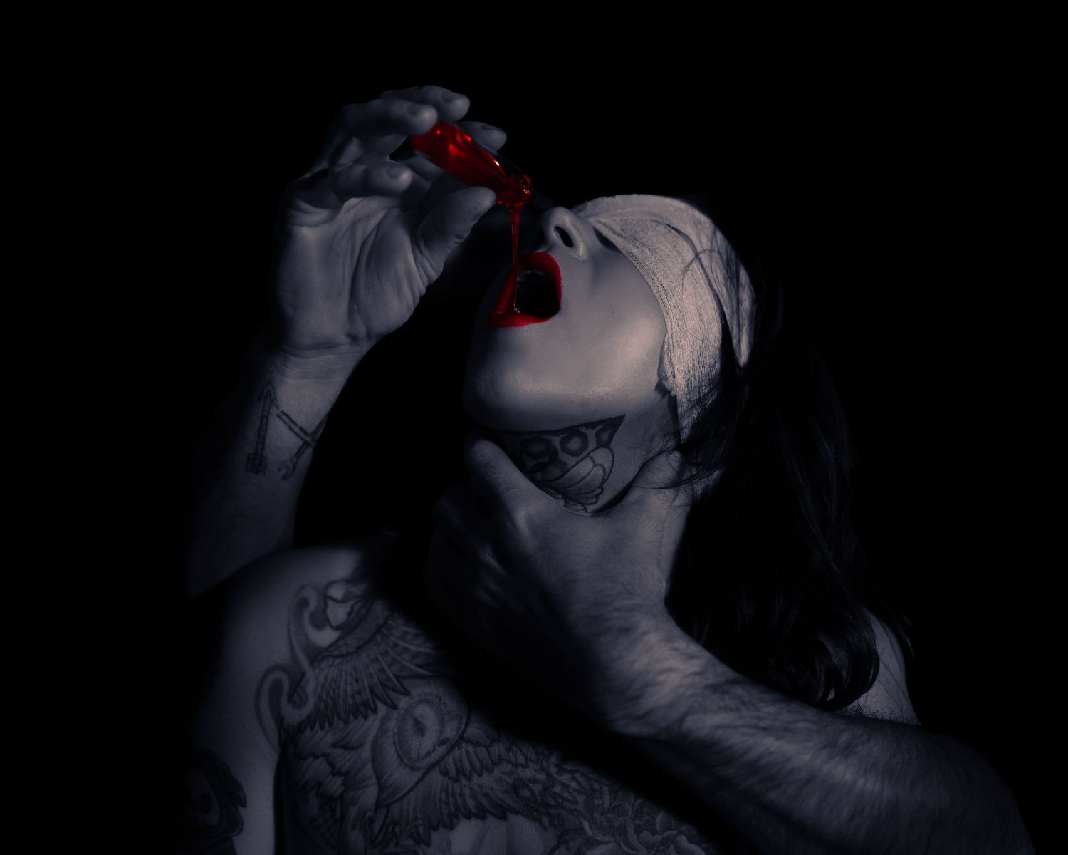 Tattooed woman in dark artistic photo holding red cherries to her lips in dramatic monochrome style.