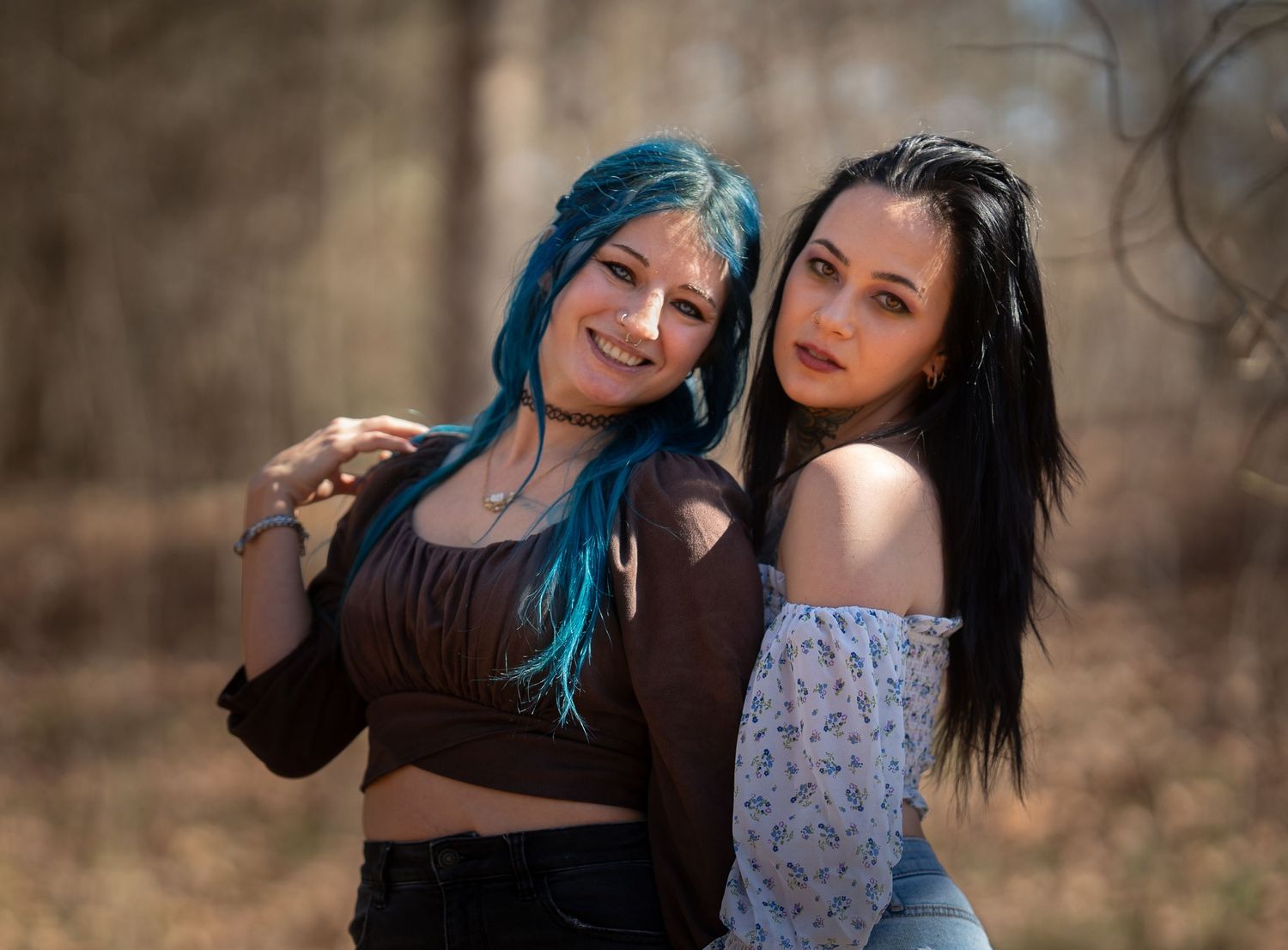 Two young women pose together outdoors, one with blue hair and one with black hair.
