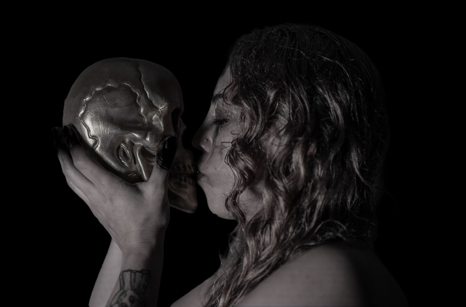 Person with long hair holding a metallic skull in a dark, dramatic black and white artistic photo.