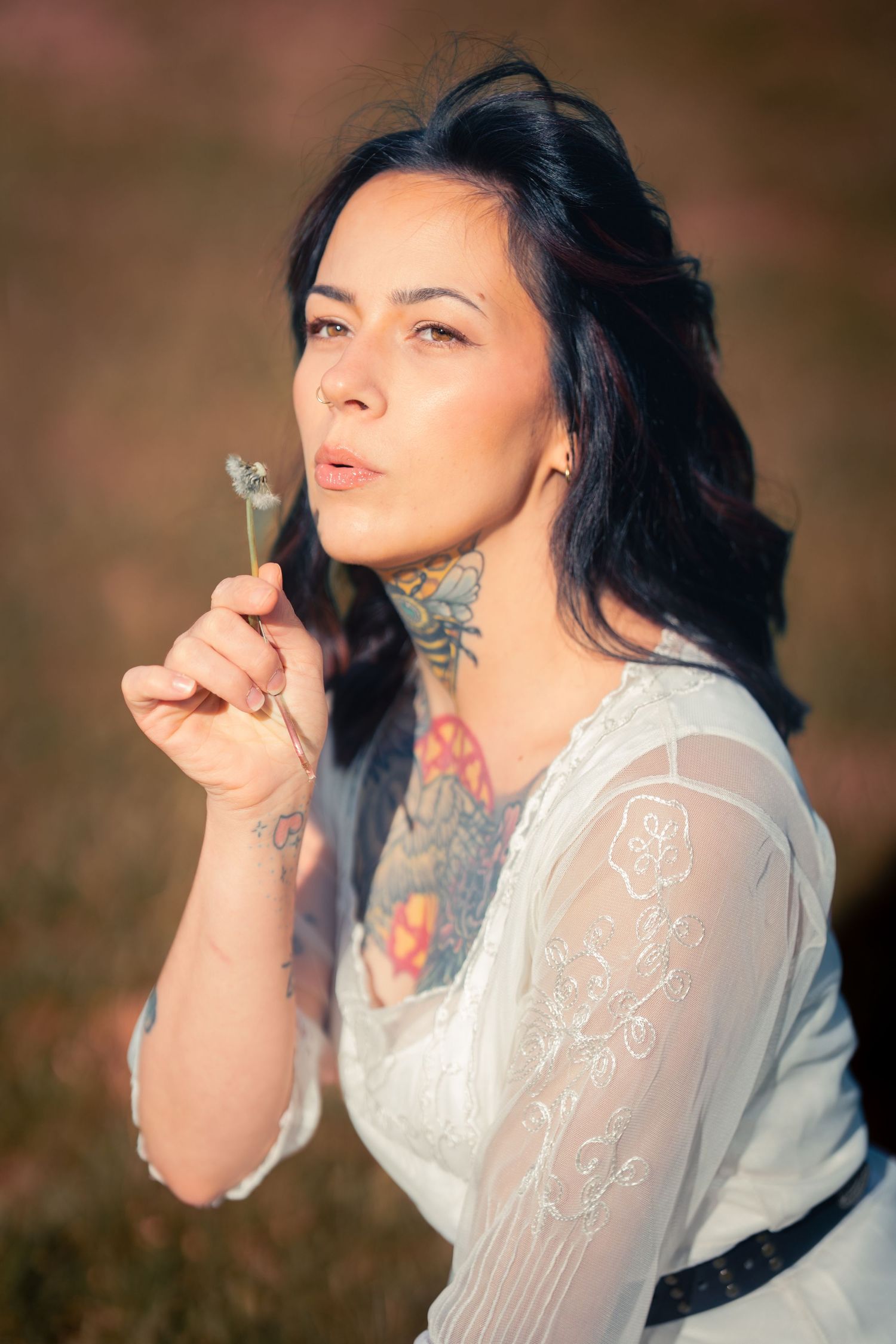 Tattooed woman in white lace dress smoking outdoors in warm golden light.
