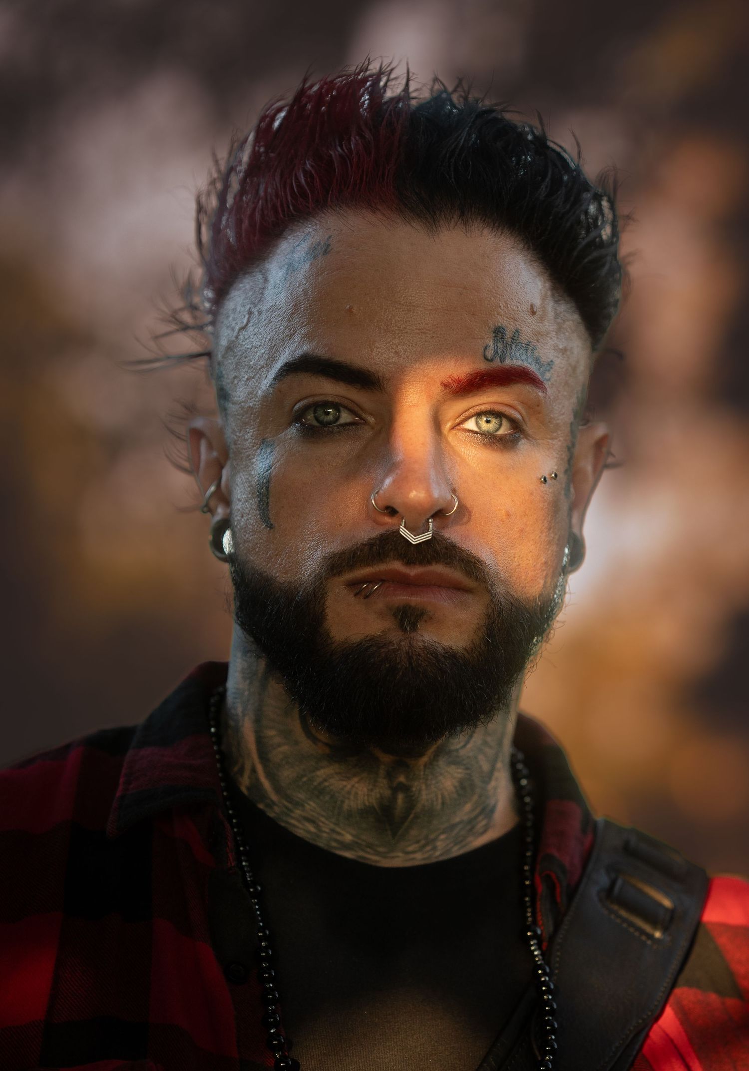 Heavily tattooed man with two-tone mohawk and facial tattoos wearing red plaid shirt outdoors.
