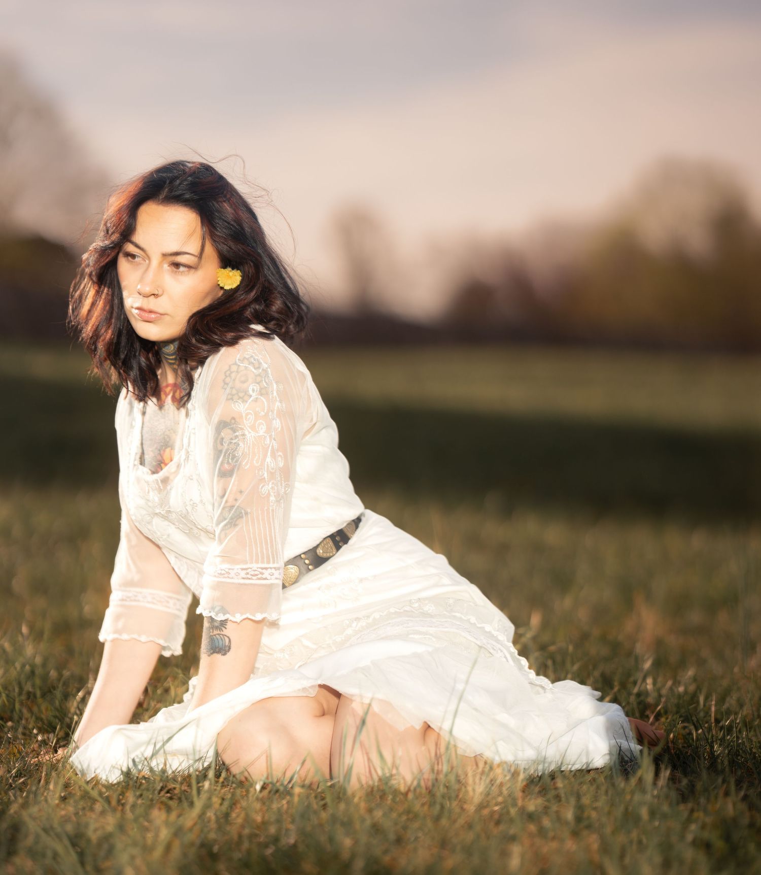 Woman in white lace dress sitting gracefully in a golden sunlit open field.