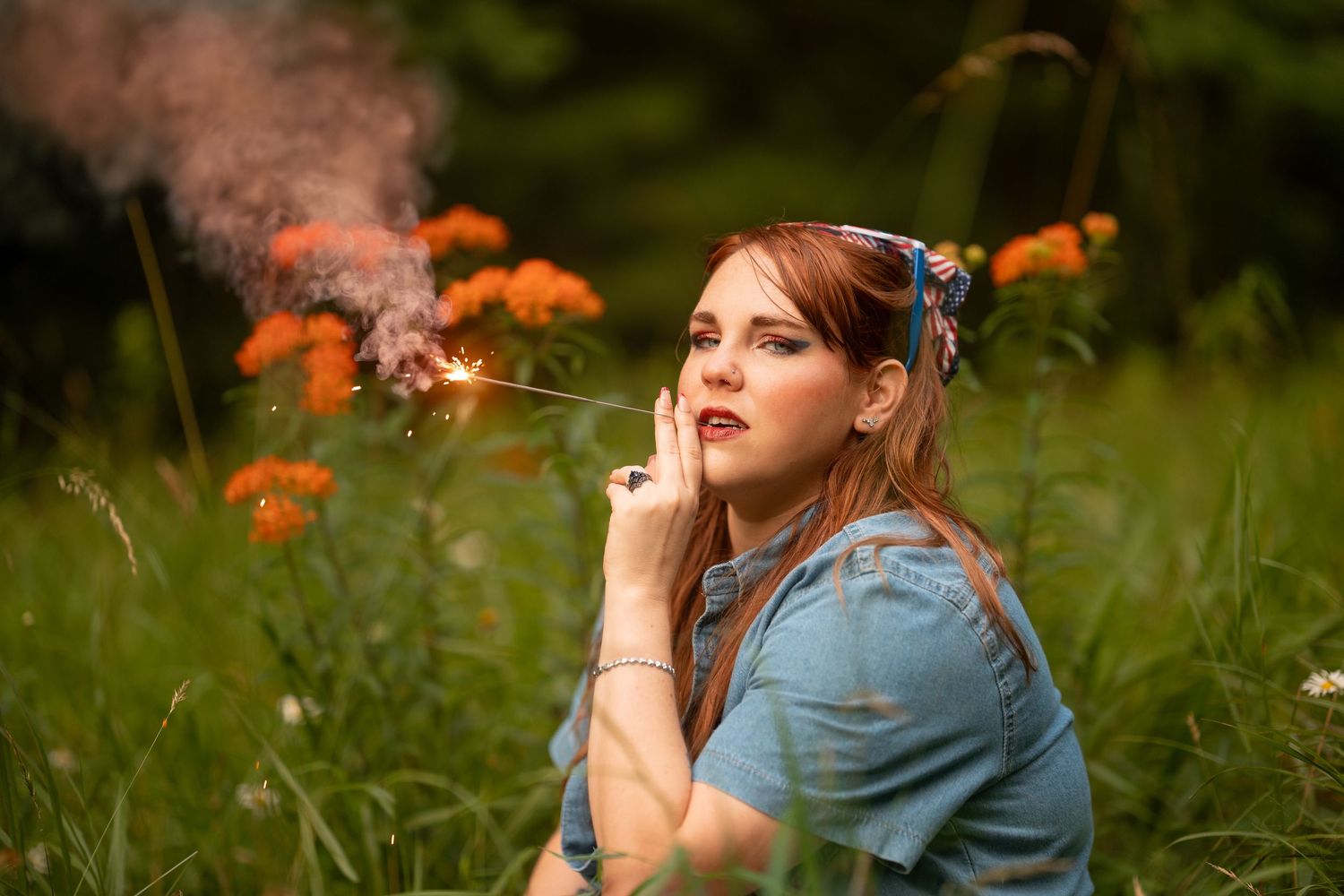 Redhead woman holding sparkler among orange wildflowers in lush green field at dusk.