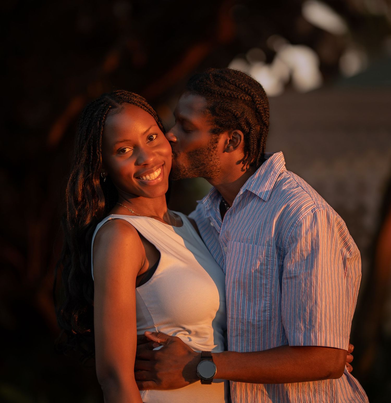 Couple sharing a romantic kiss outdoors in warm golden light at dusk.