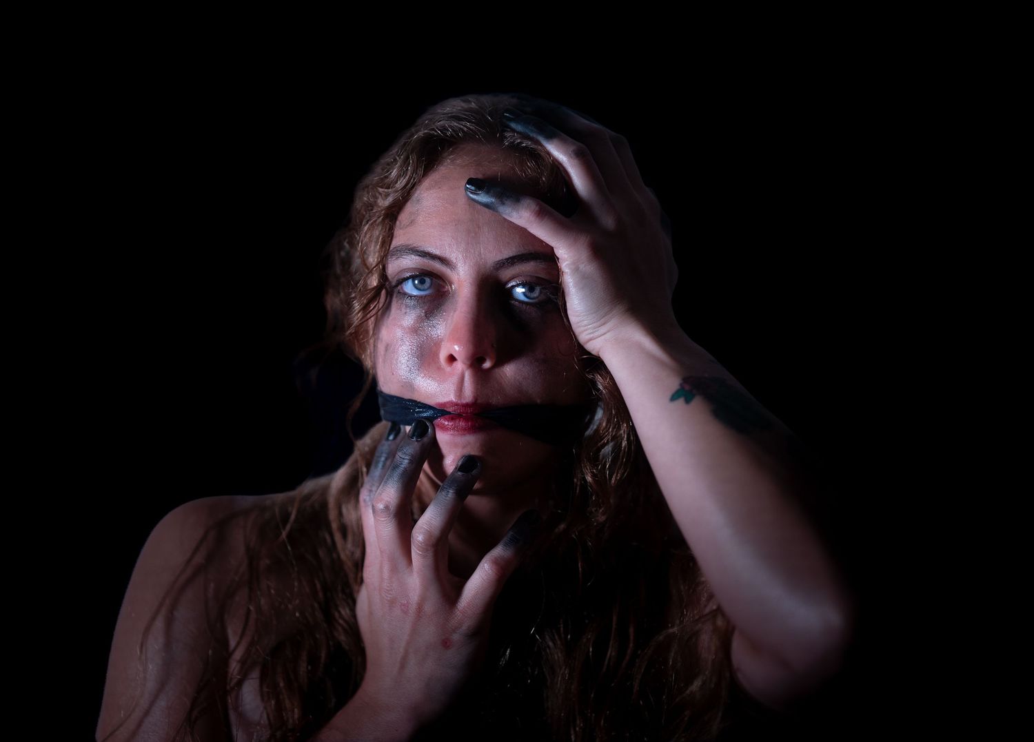 Woman with wide eyes and dark makeup holds her face dramatically against a black background.