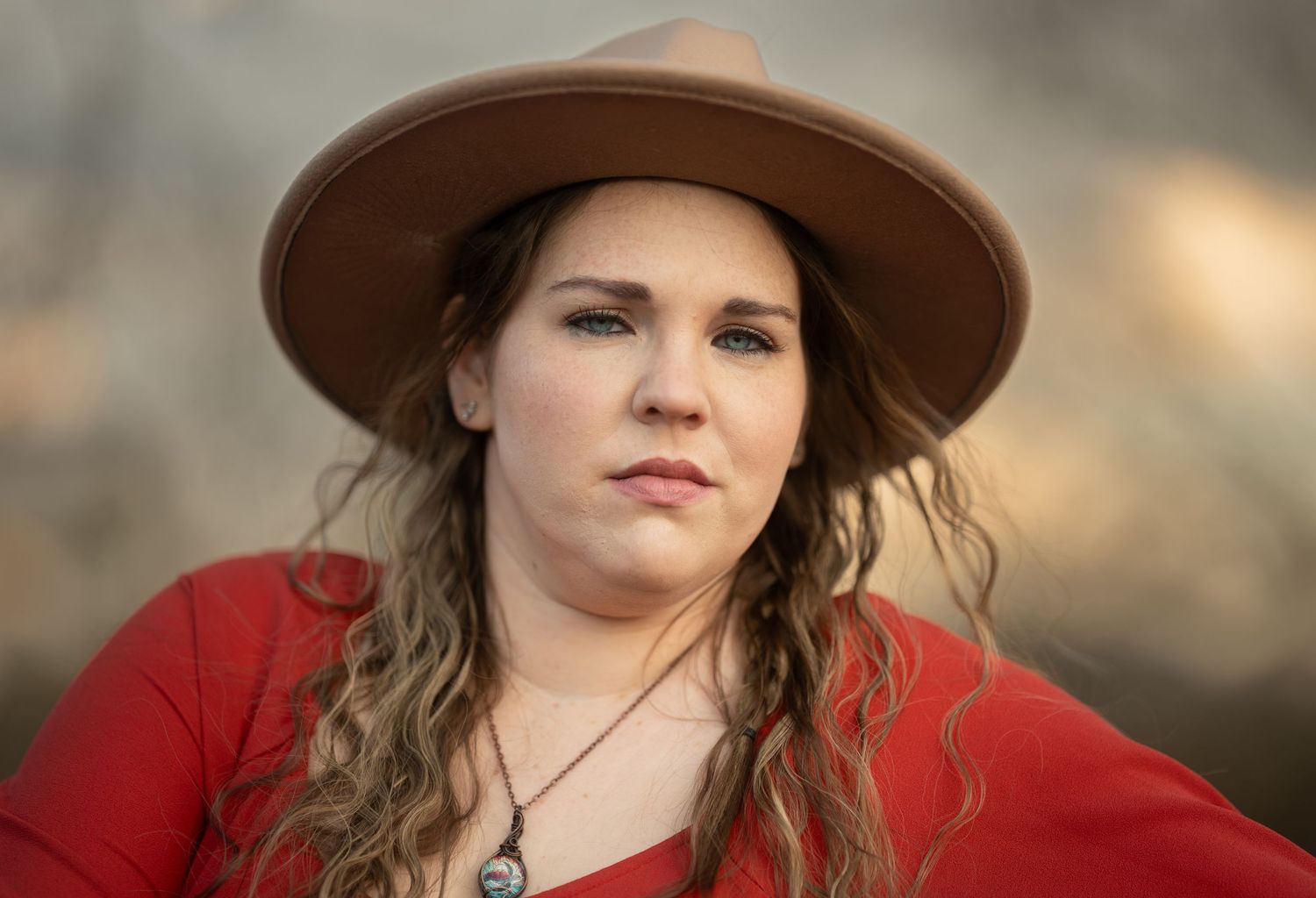 Close-up portrait of woman in red top and tan wide-brim hat with wavy hair.