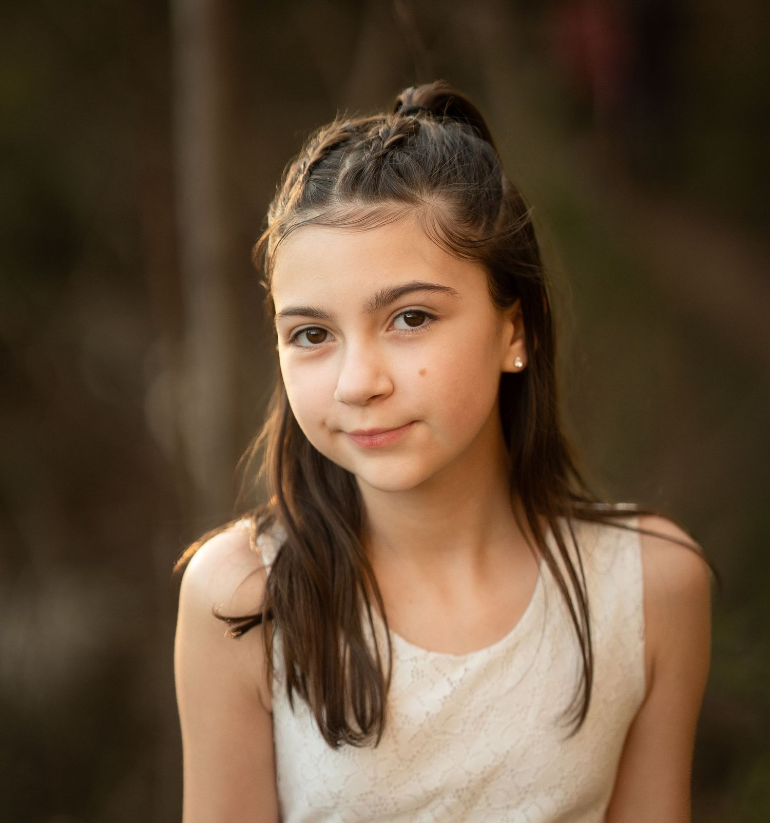 Pretty young girl with half-up braided hairstyle smiles softly in warm outdoor portrait.